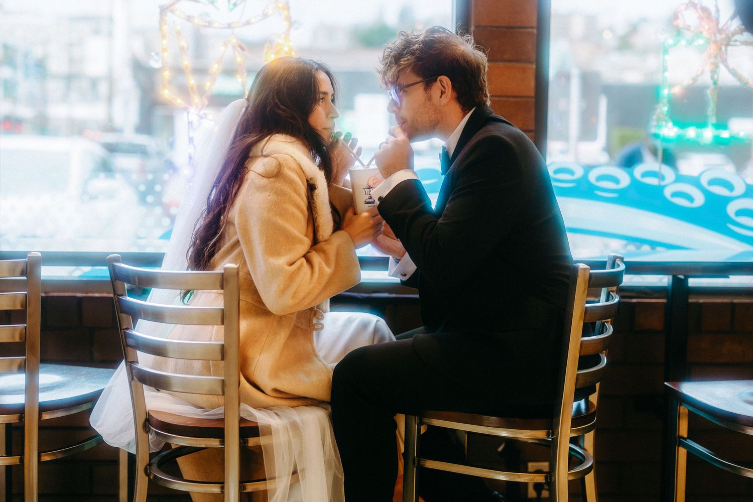 Two people sit at a coffee shop table near a window having a conversation.