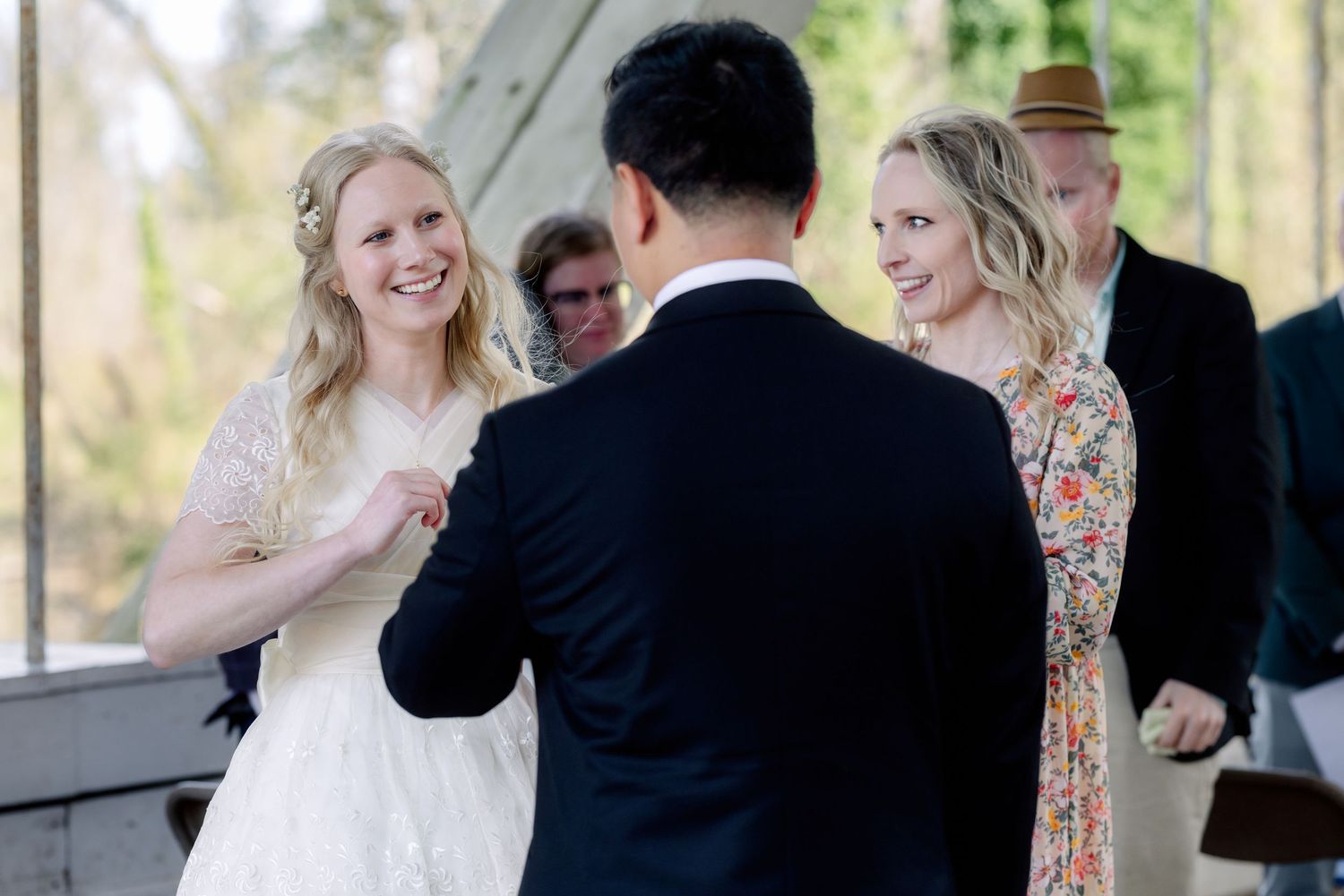 Smiling bride in white lace dress exchanges vows with groom at outdoor wedding ceremony.