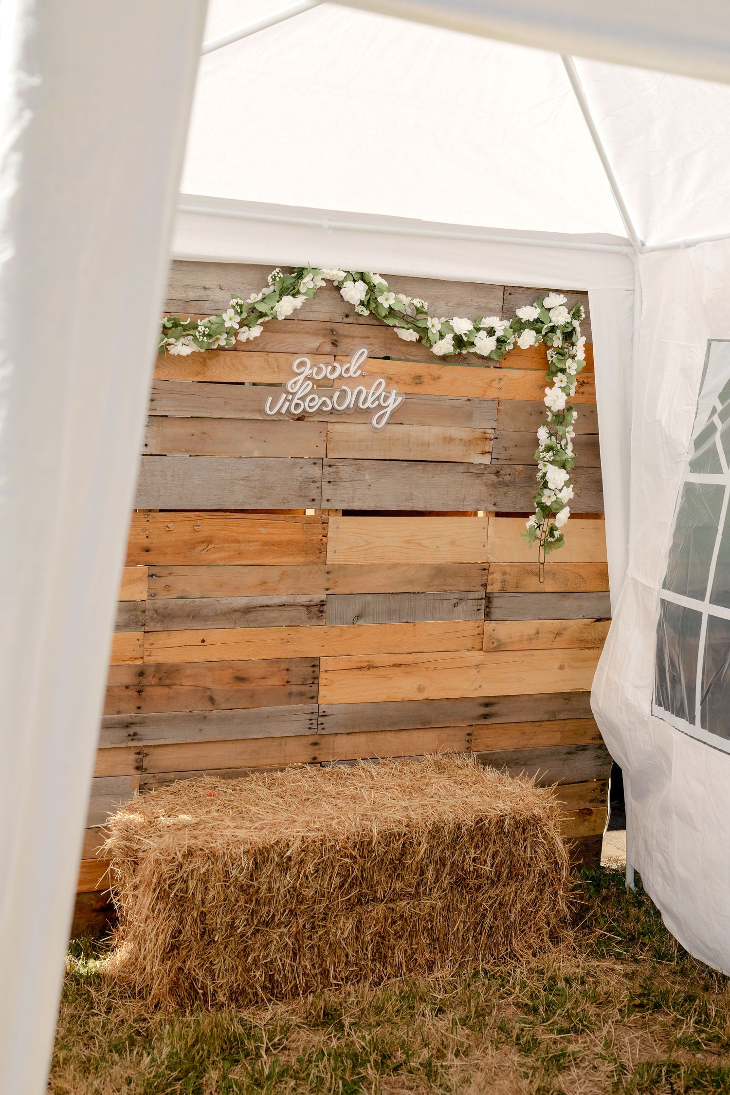 Rustic wooden pallet photo booth backdrop with floral garland and good vibes only sign at outdoor wedding.