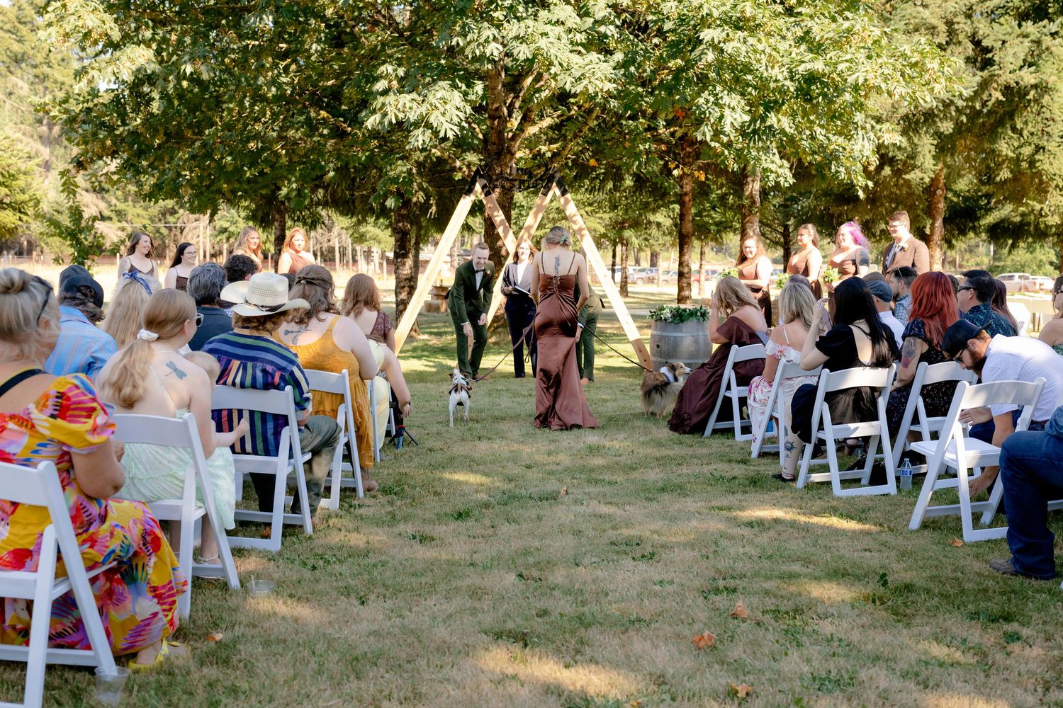 Outdoor wedding ceremony with guests seated on white chairs facing couple at a triangular wooden arch altar.