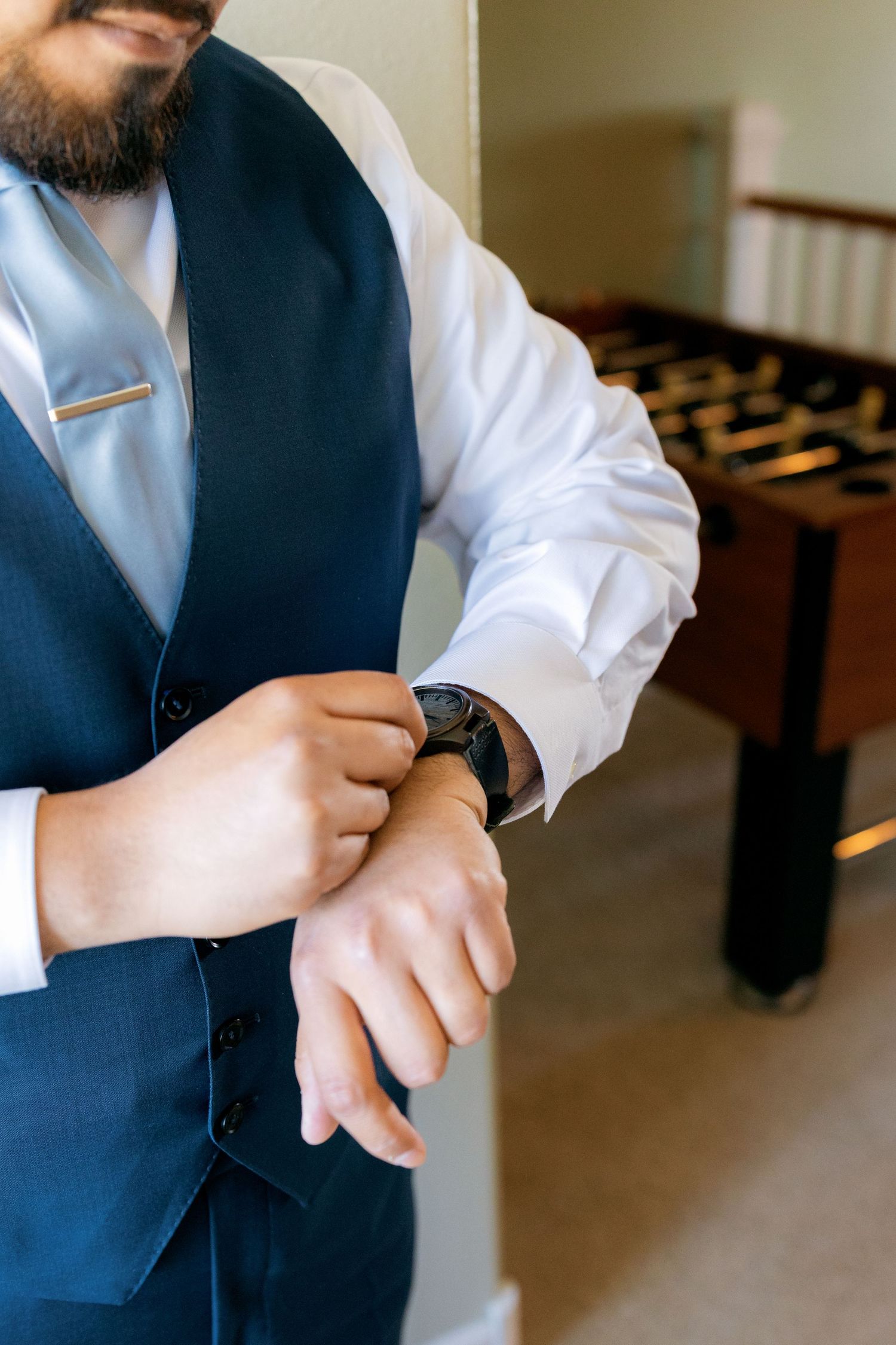 Bearded groom in navy vest adjusting his watch while getting ready for his wedding day.