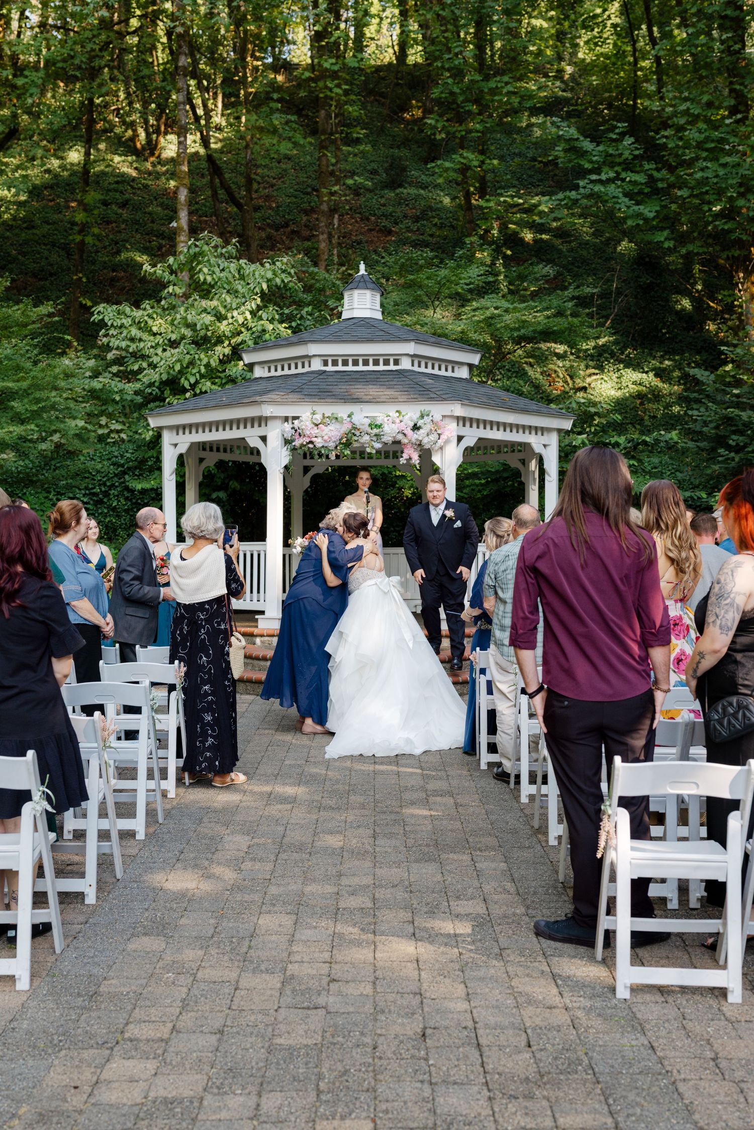 Bride and groom walking back down aisle after wedding ceremony at white gazebo surrounded by trees.