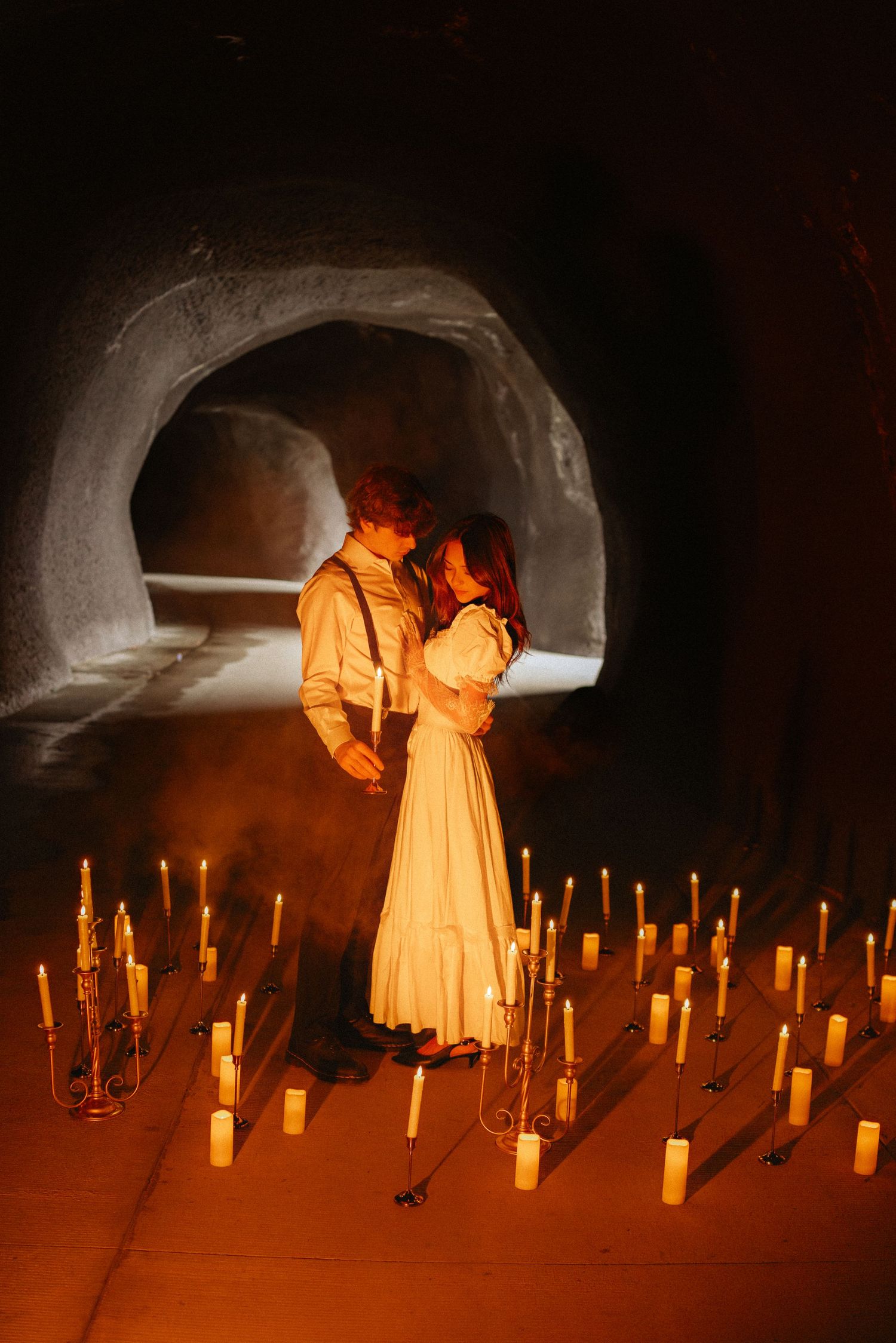 Figures in flowing dresses move through a candlelit tunnel creating an ethereal scene.