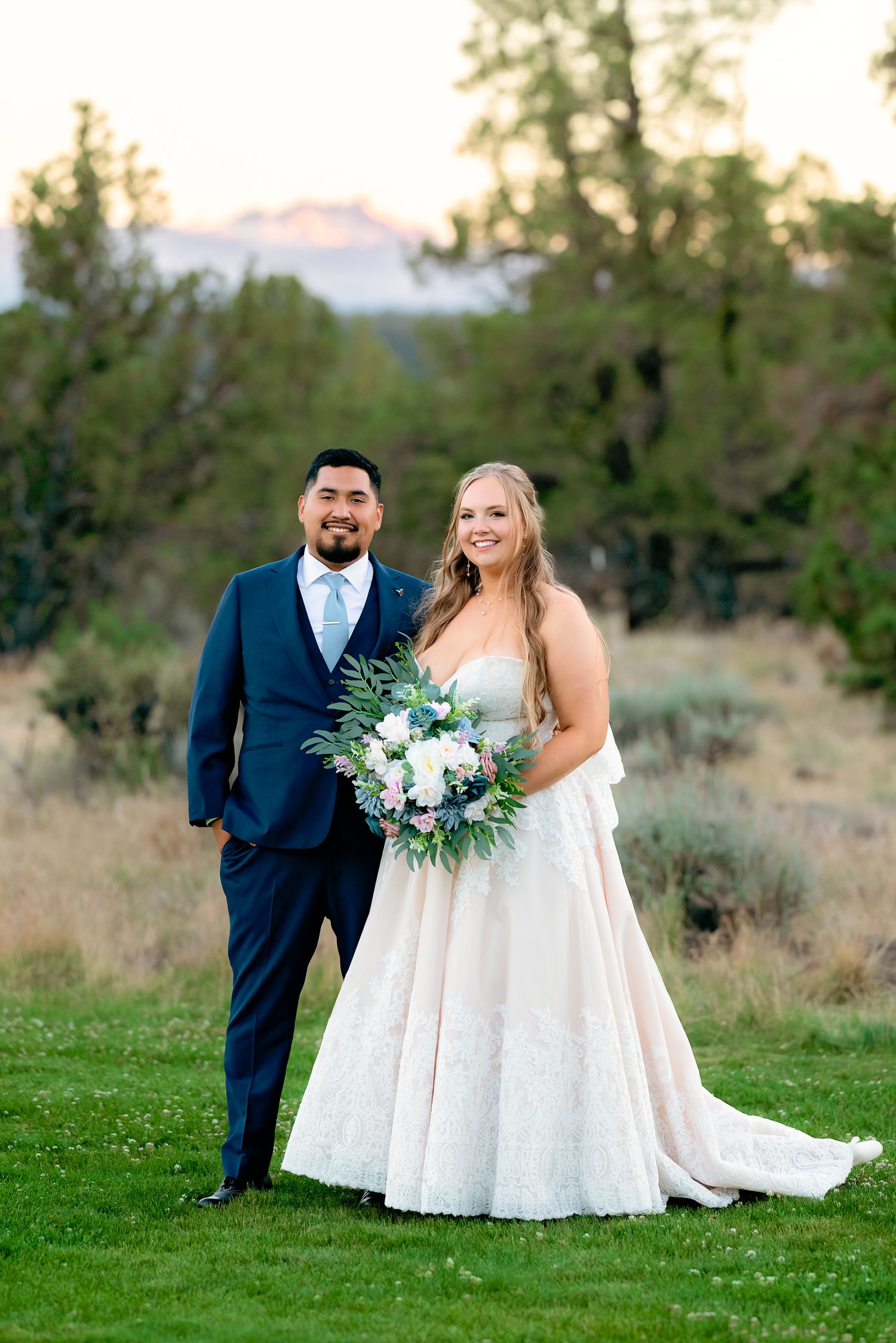 Bride and groom portrait at sunset with mountain backdrop, bride holding white and blush bouquet.