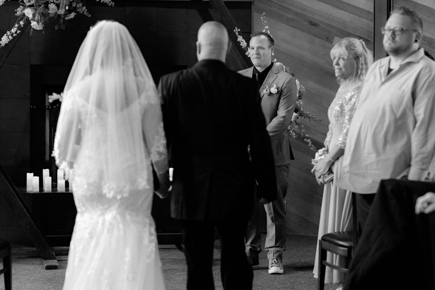 Black and white photo of a bride walking down the aisle toward the groom at a wedding ceremony.