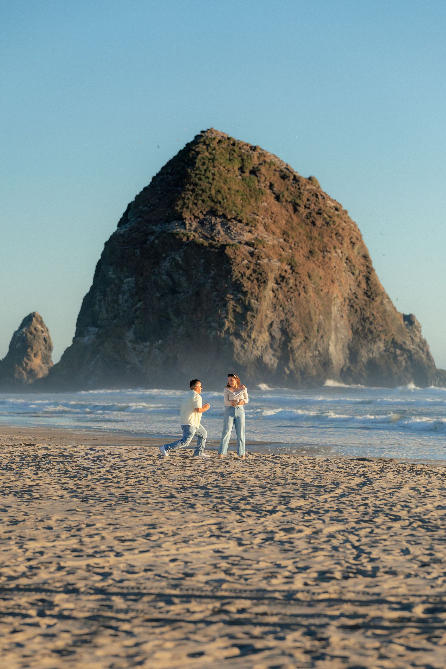 Couple walking on Cannon Beach with iconic Haystack Rock in the background during golden hour.