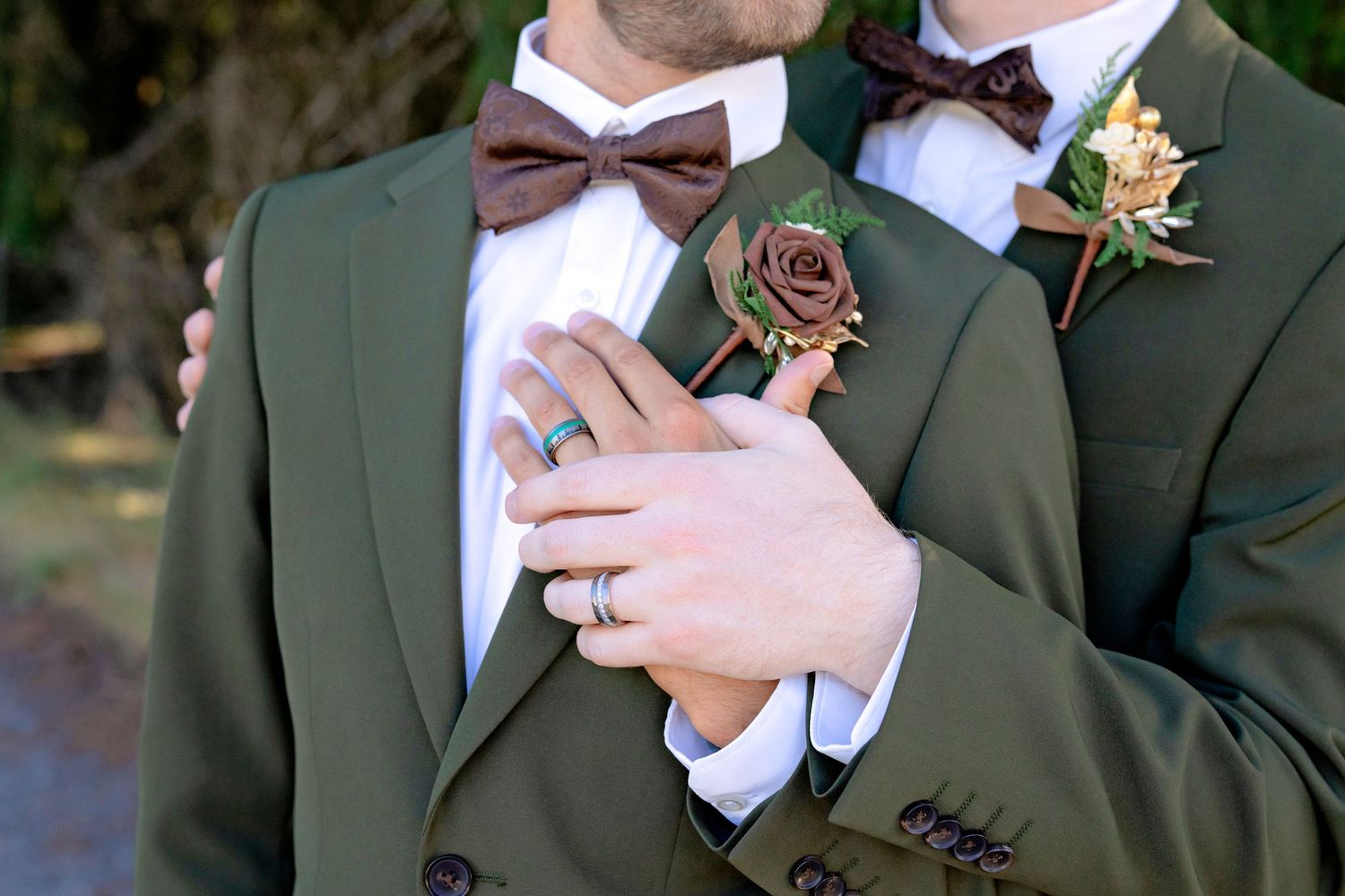 Two grooms in olive green suits with brown bow ties and rose boutonnieres at a wedding ceremony.