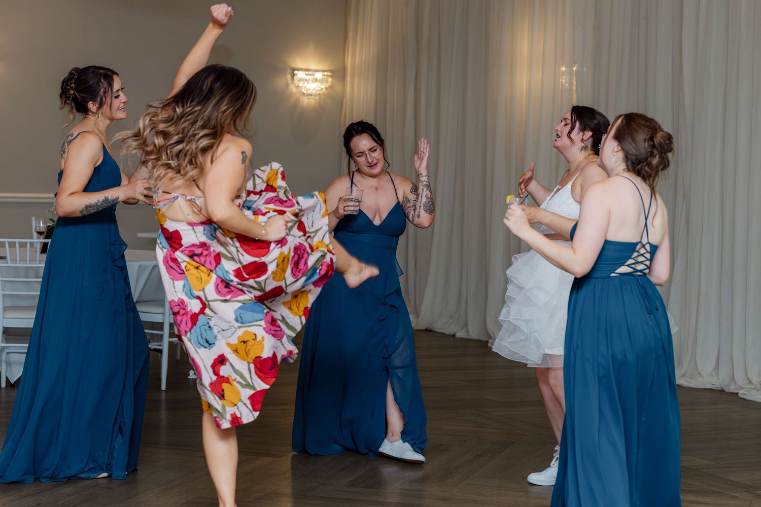 Bridesmaids in teal gowns and guests dancing joyfully at a wedding reception on the dance floor.