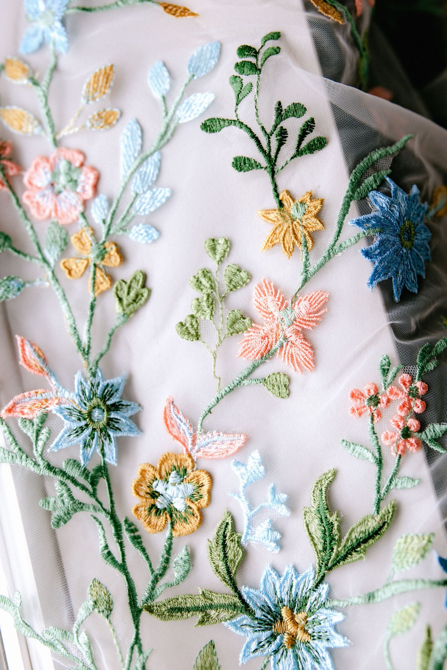 Colorful floral embroidery on white wedding veil with pastel flowers.