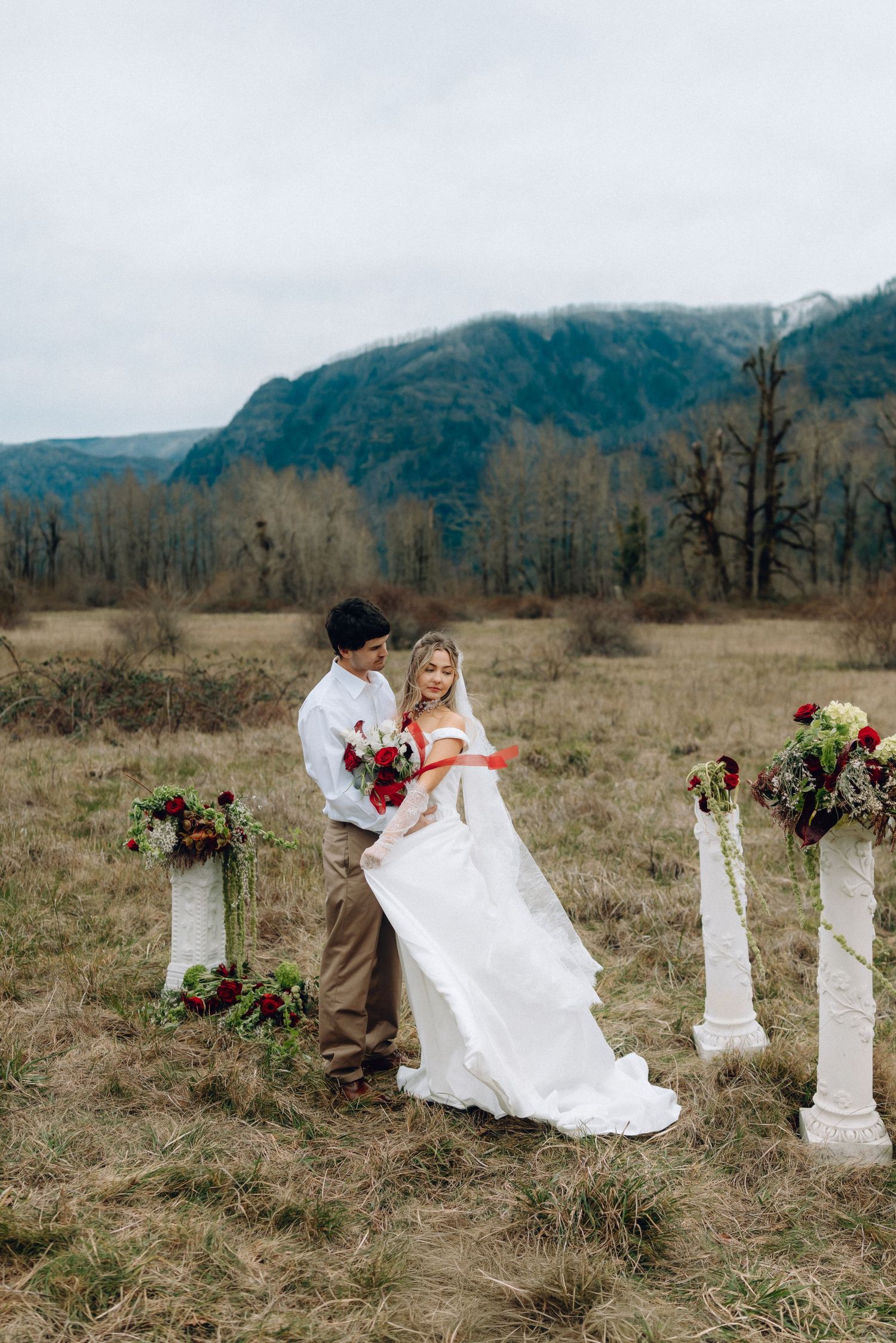 A romantic wedding dance dip pose among decorative white pillars in a mountain field setting.