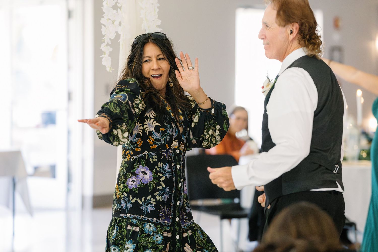 Wedding guests dancing and celebrating at indoor reception with festive lighting.