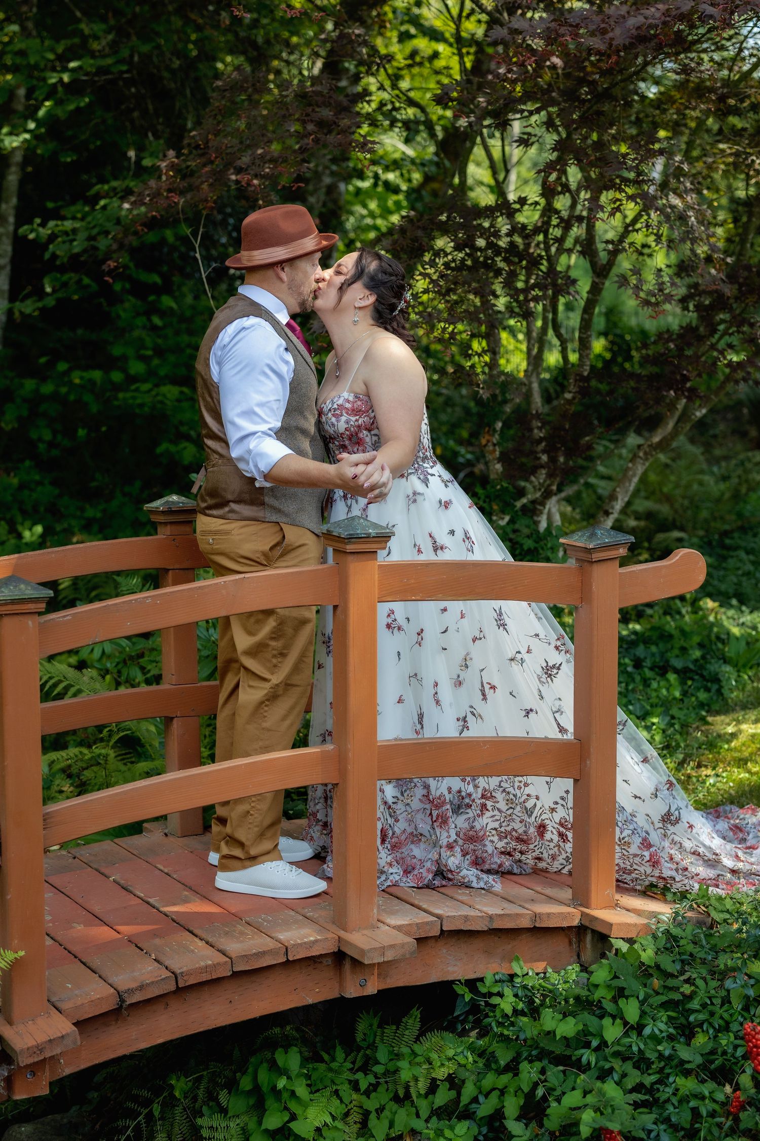A romantic moment shared on a wooden garden bridge surrounded by lush greenery.