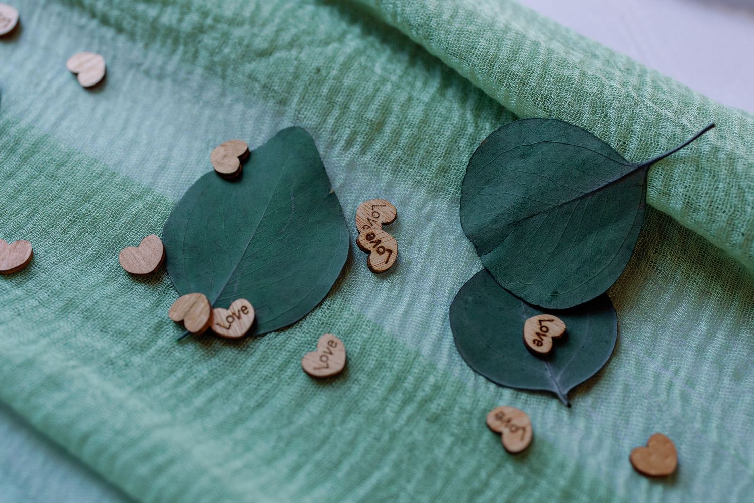 Small wooden heart decorations arranged on mint green fabric with delicate scattered pattern.
