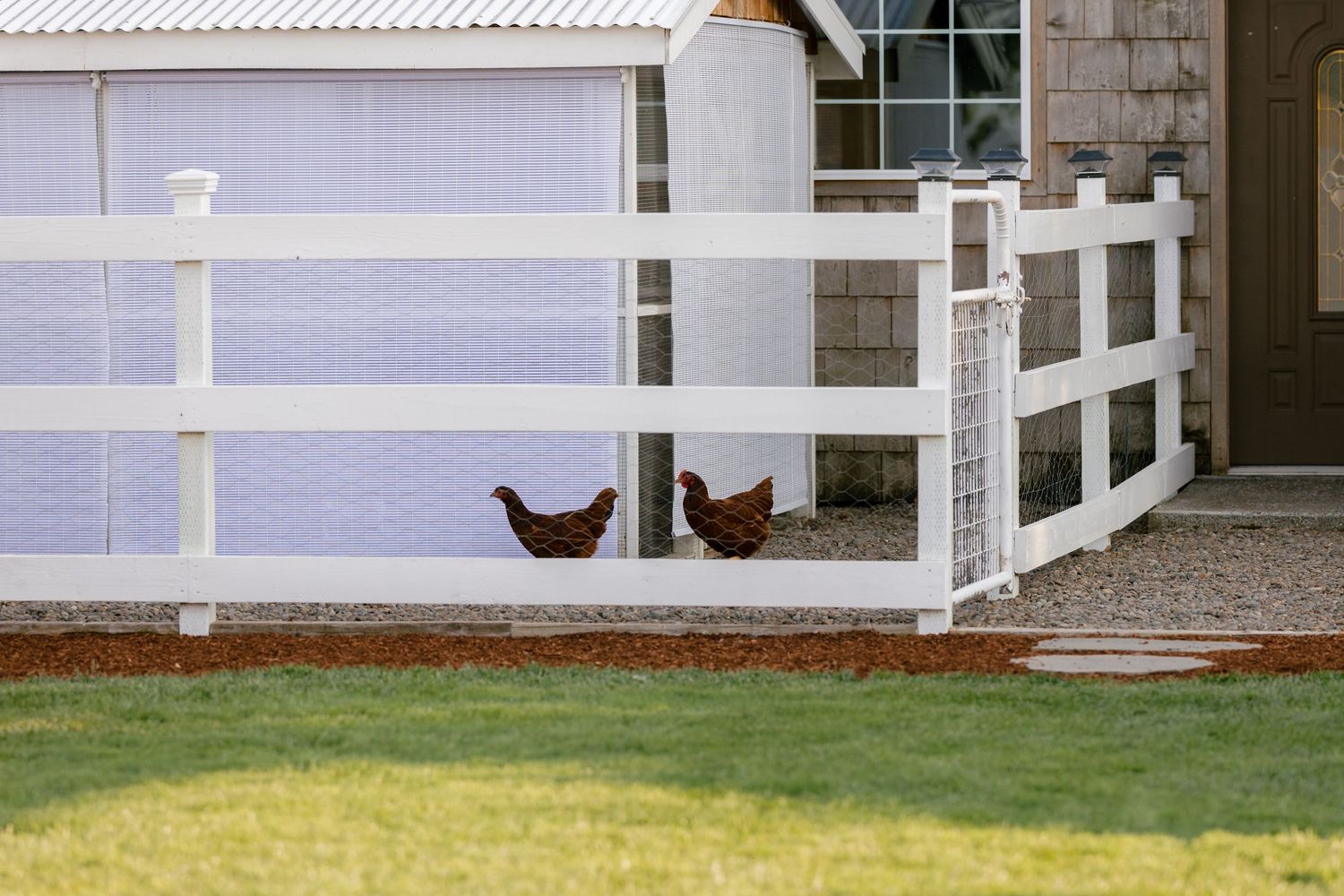 White picket fence surrounding a residential property with green grass and landscaping.