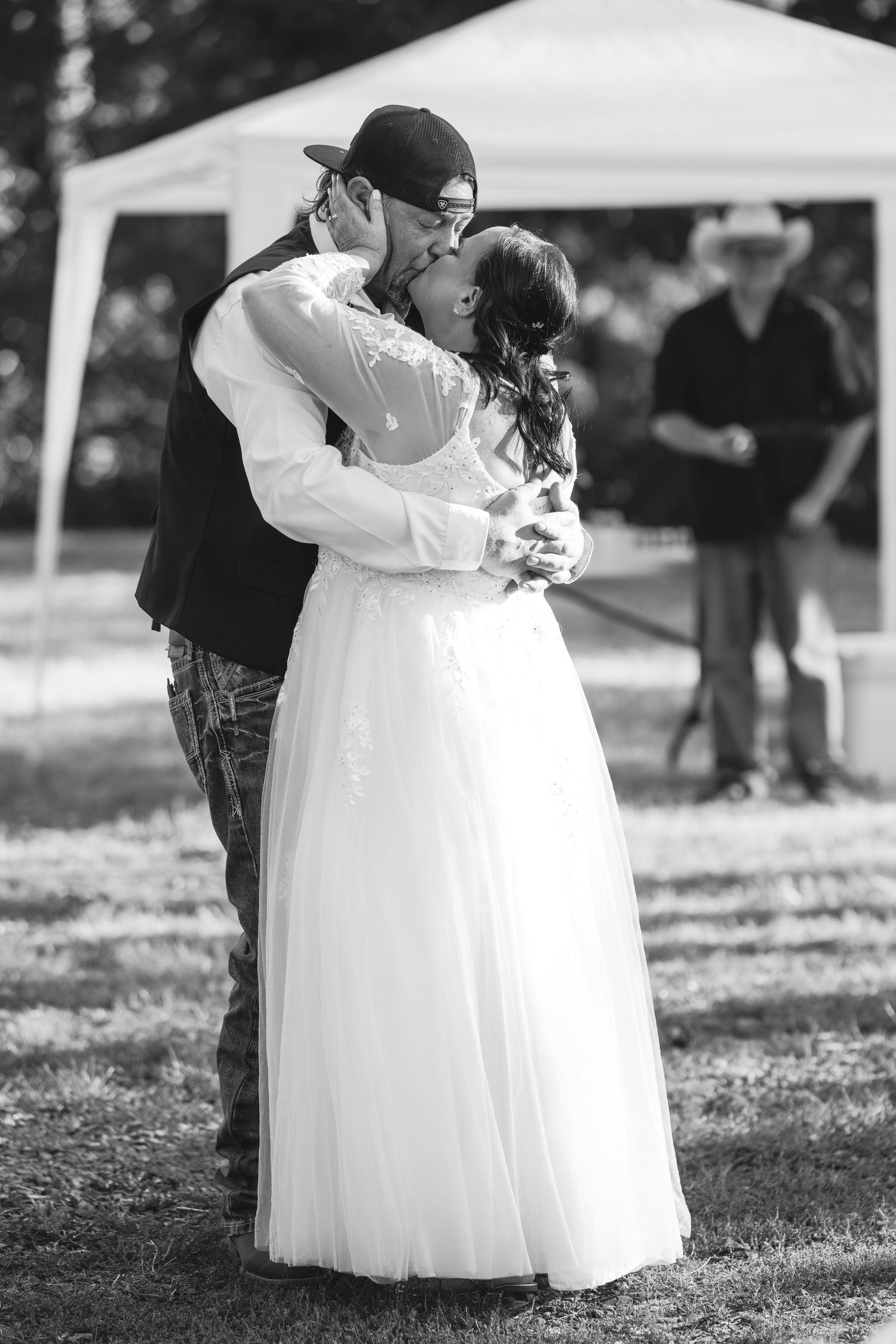 A black and white photo captures an intimate moment between newlyweds during an outdoor wedding celebration.