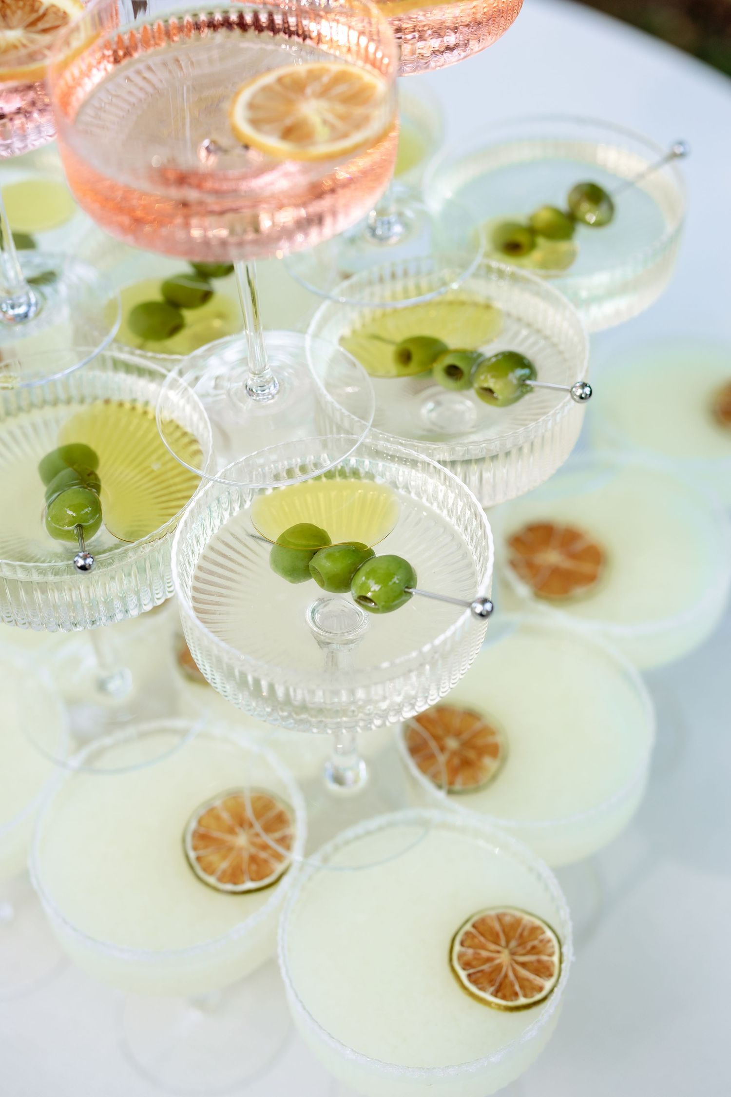 Elegant cocktail glasses arranged with citrus slices and green garnishes on a white surface for an upscale event.