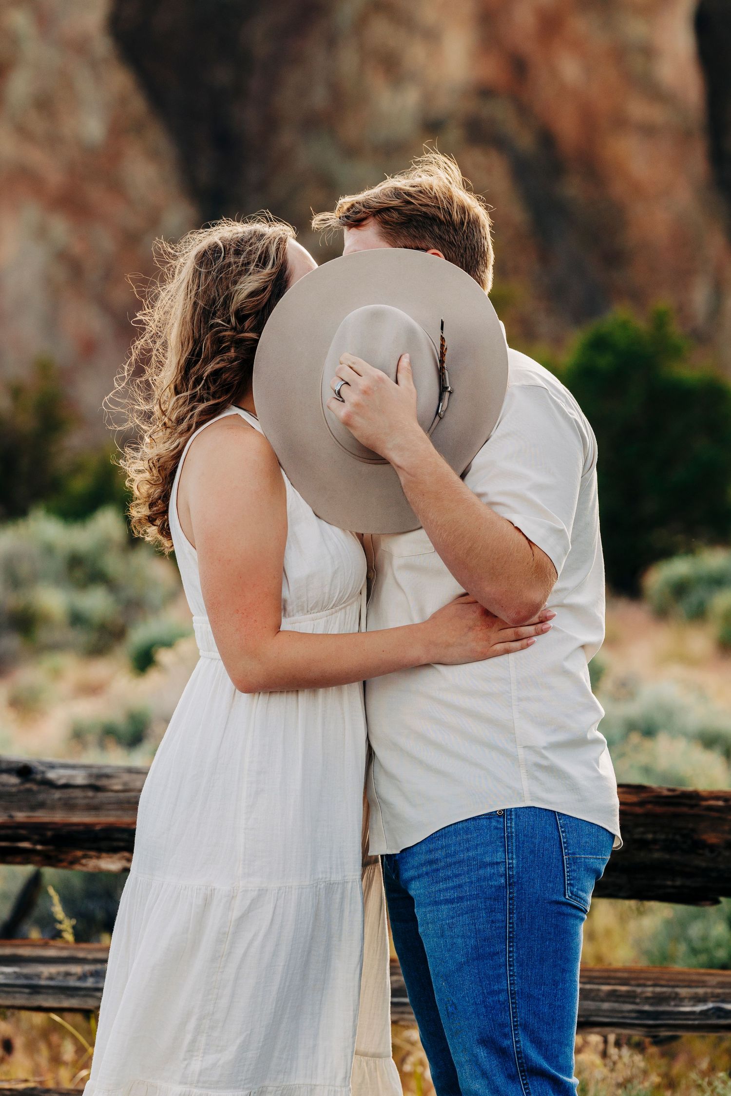 A romantic couple embraces at sunset against a backdrop of red sandstone cliffs in a scenic desert landscape.
