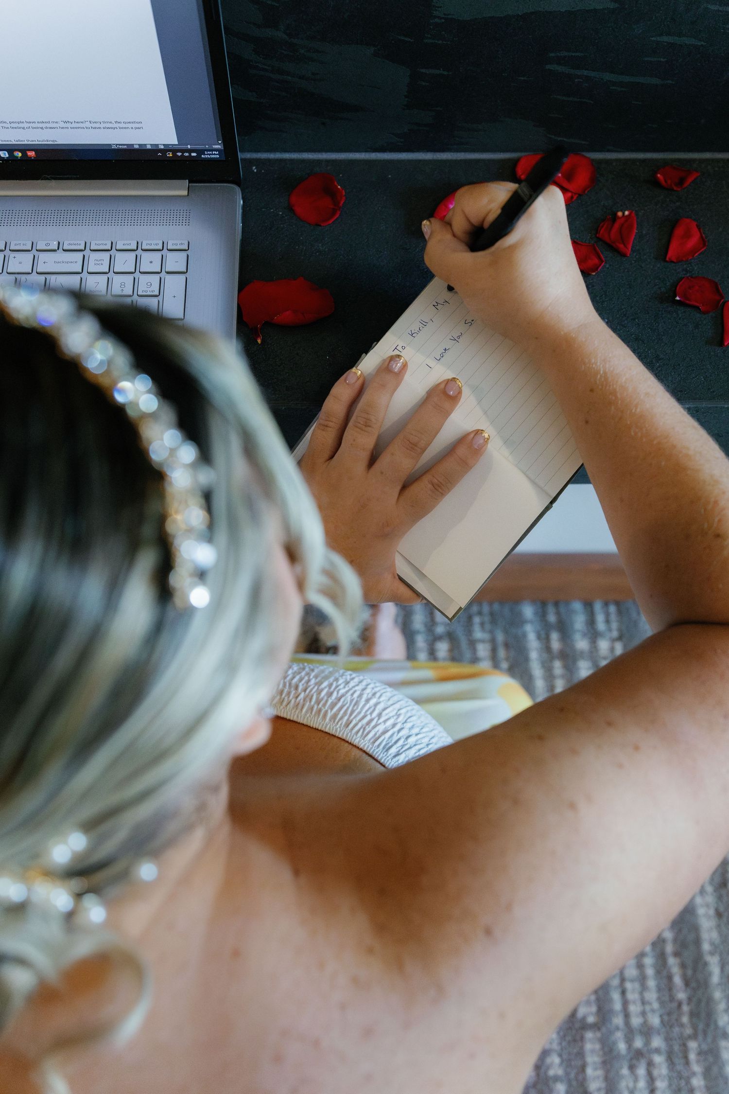 Close-up view of hands writing on paper with red rose petals scattered on a desk.