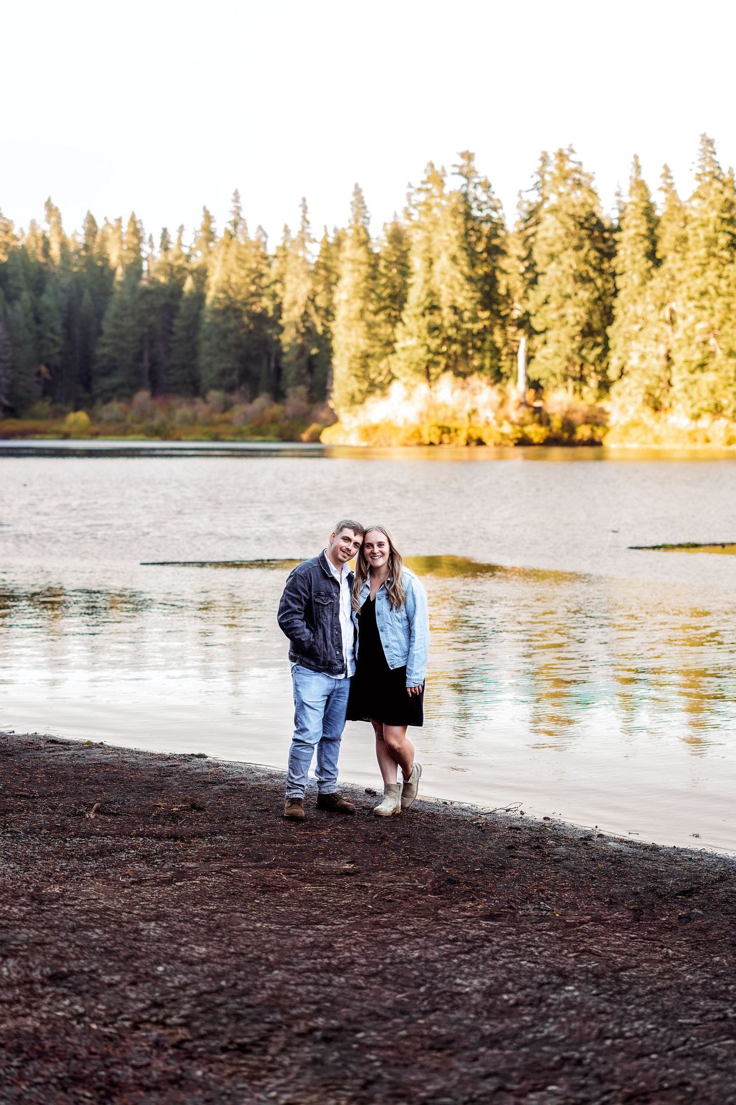 A romantic lakeside moment at sunset with pine trees reflecting on calm waters.