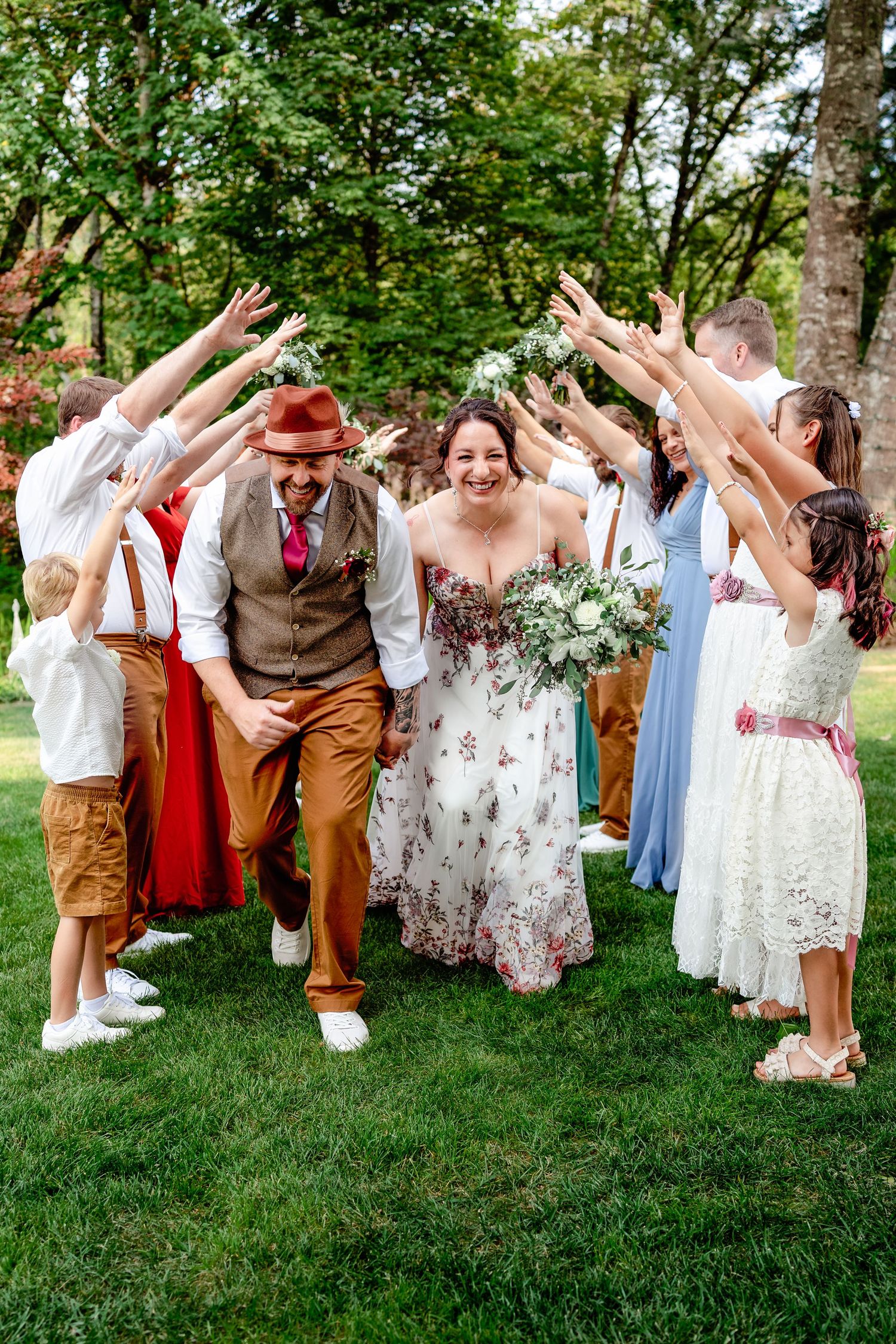 Joyful wedding party celebration with raised hands on a sunny garden lawn.