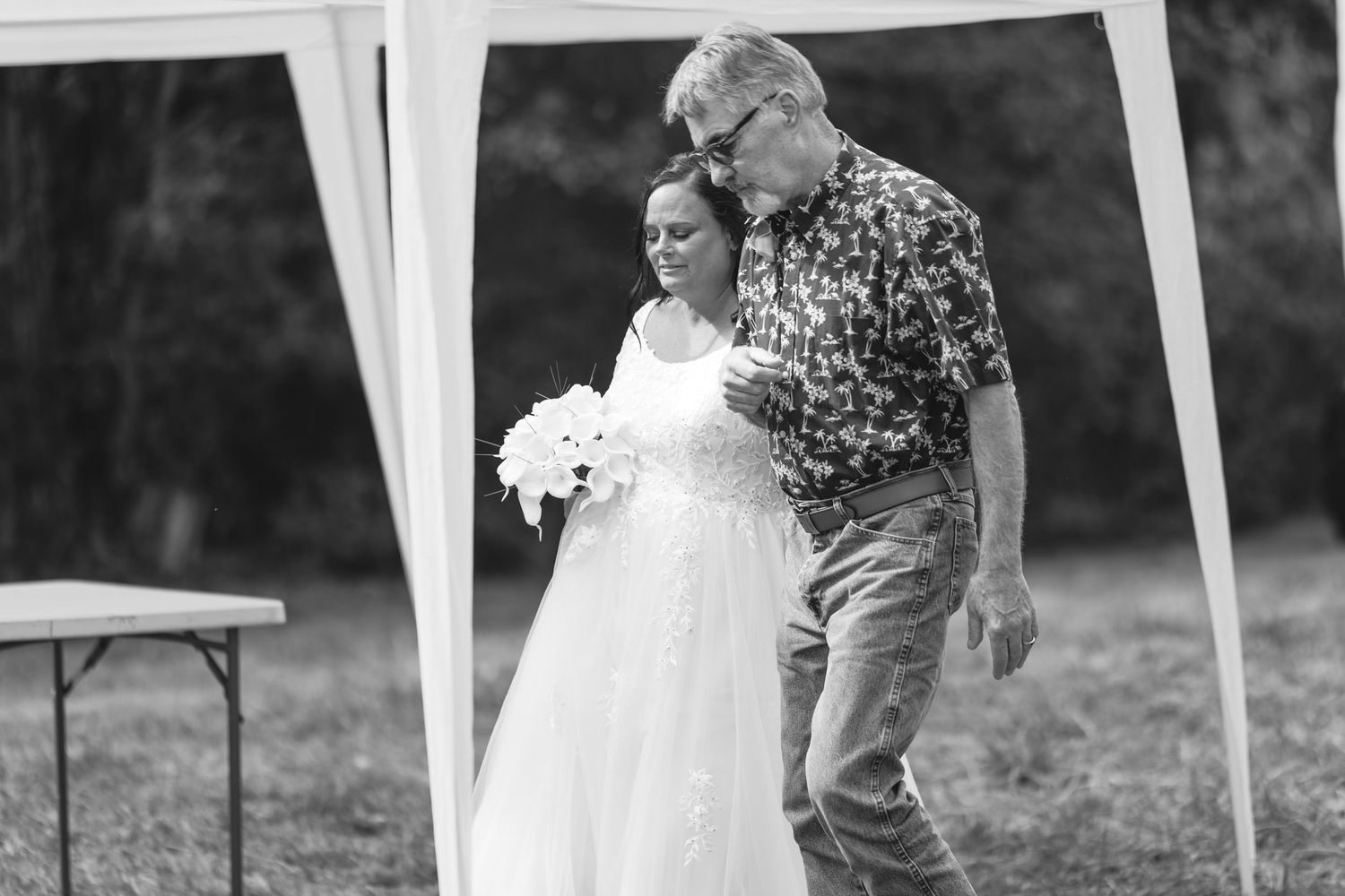 Black and white wedding photo showing a couple walking under an outdoor tent with guests seated at tables.