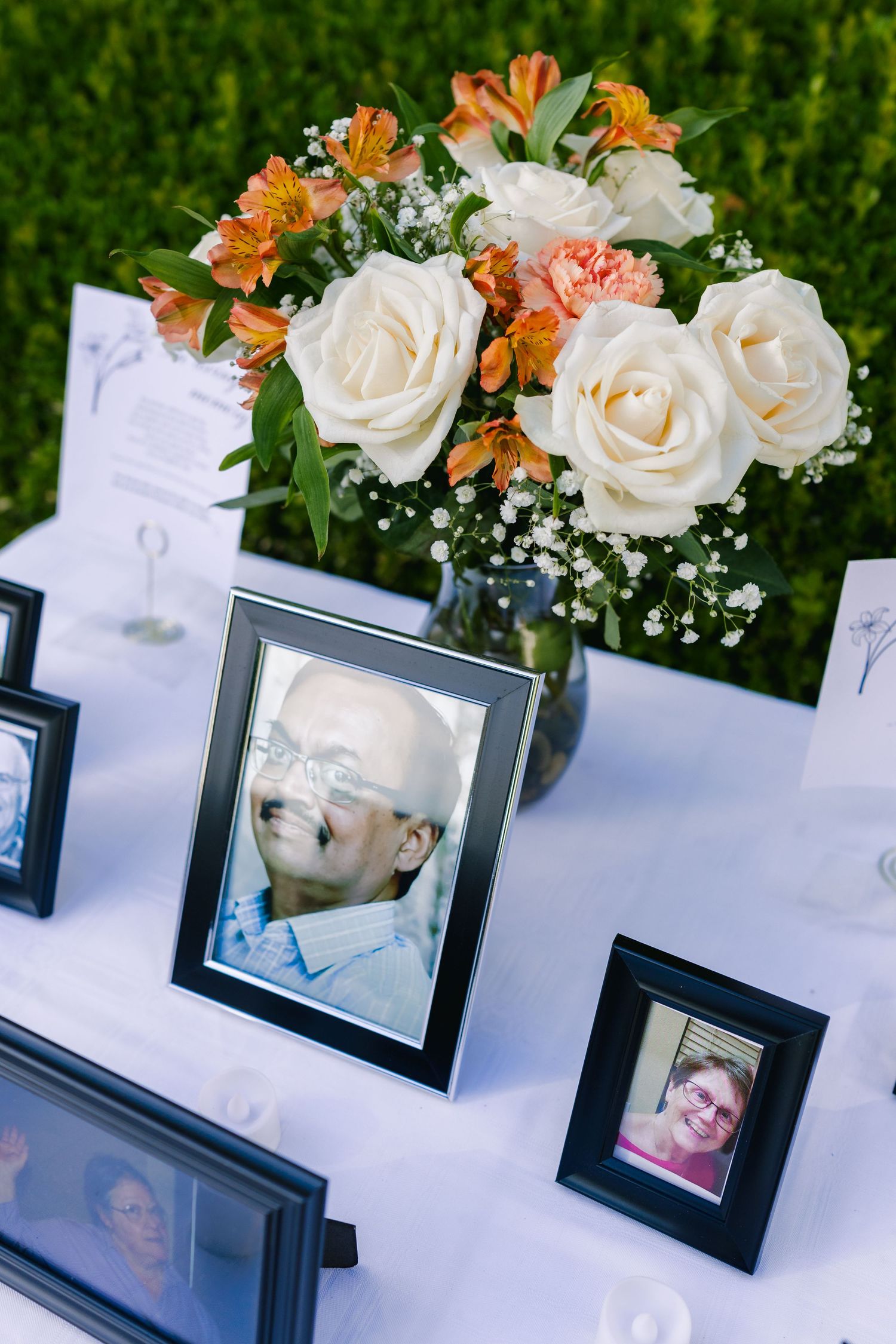 Wedding table decorations feature white roses and orange lilies in vases alongside framed photos.