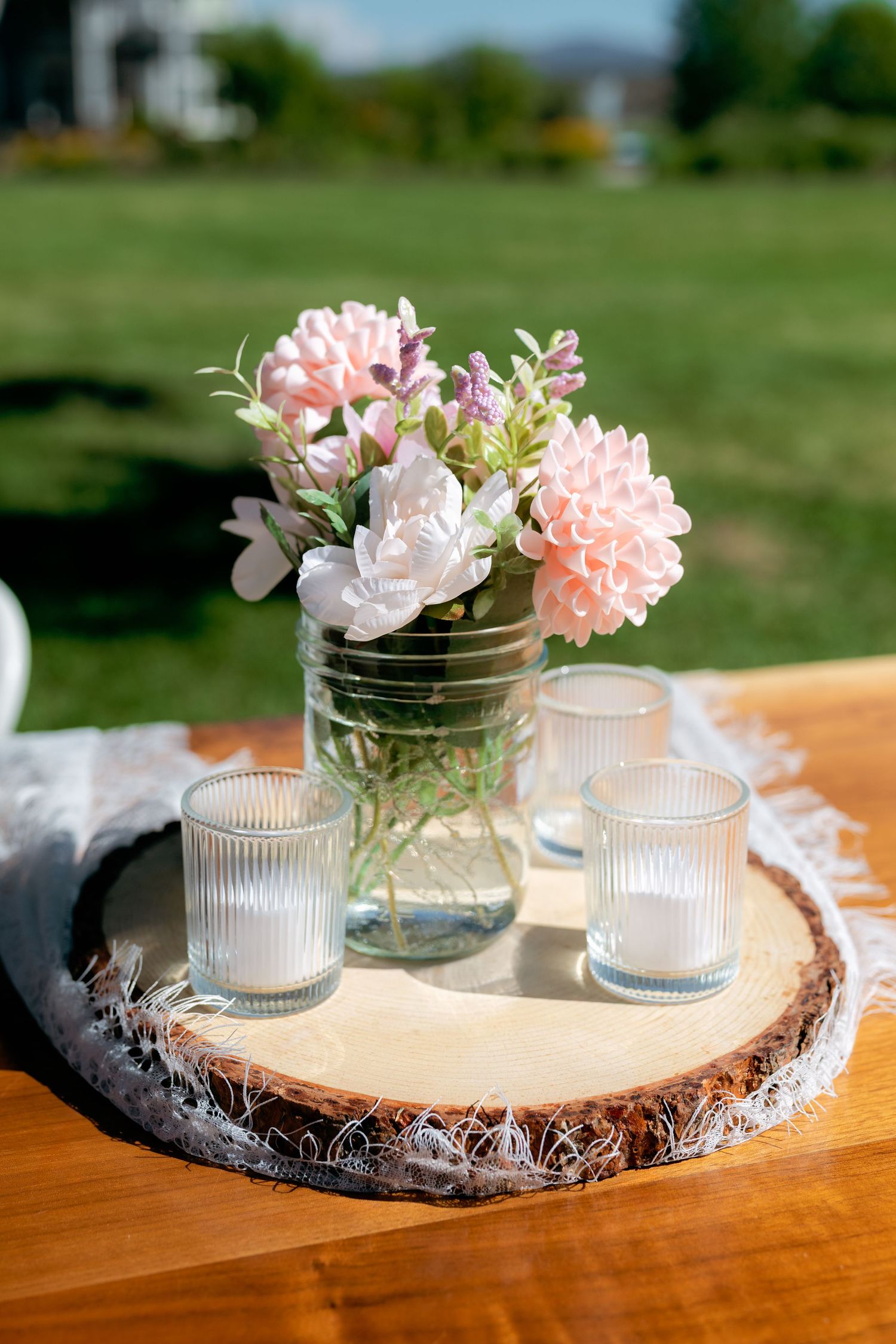 Rustic wedding centerpiece with pink and white flowers in a mason jar with votive candles on a wood slice.