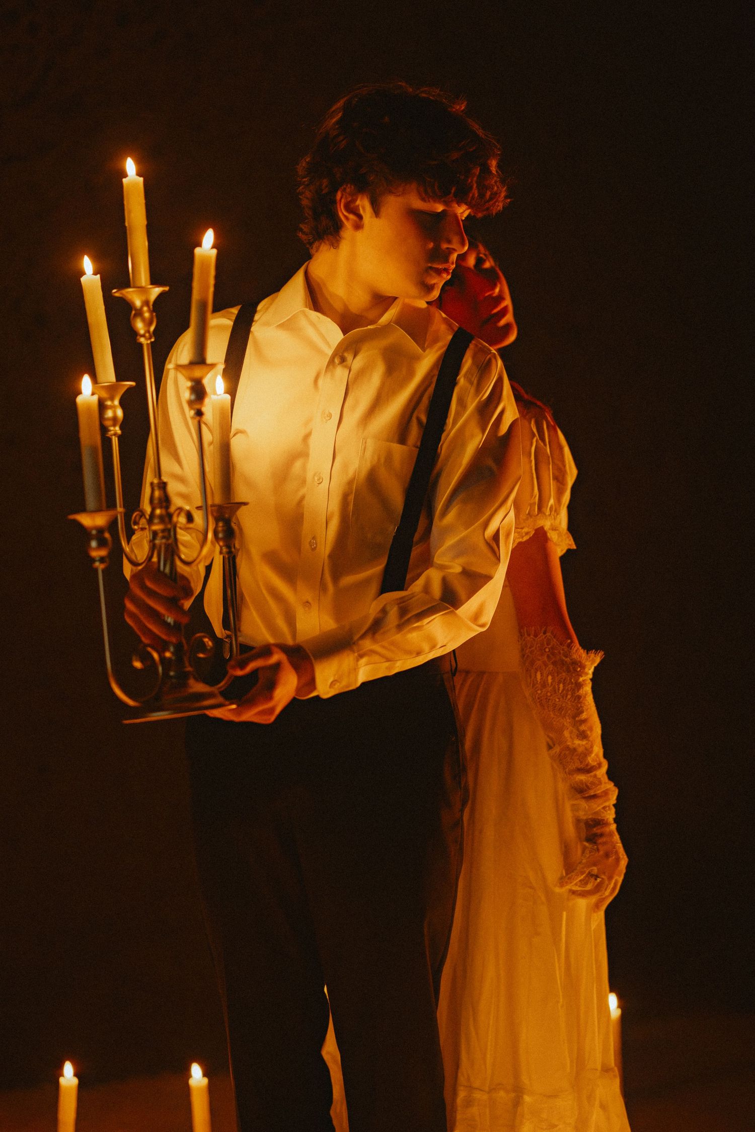 A figure in a white dress holds a vintage candelabra in a dark moody setting with warm candlelight.
