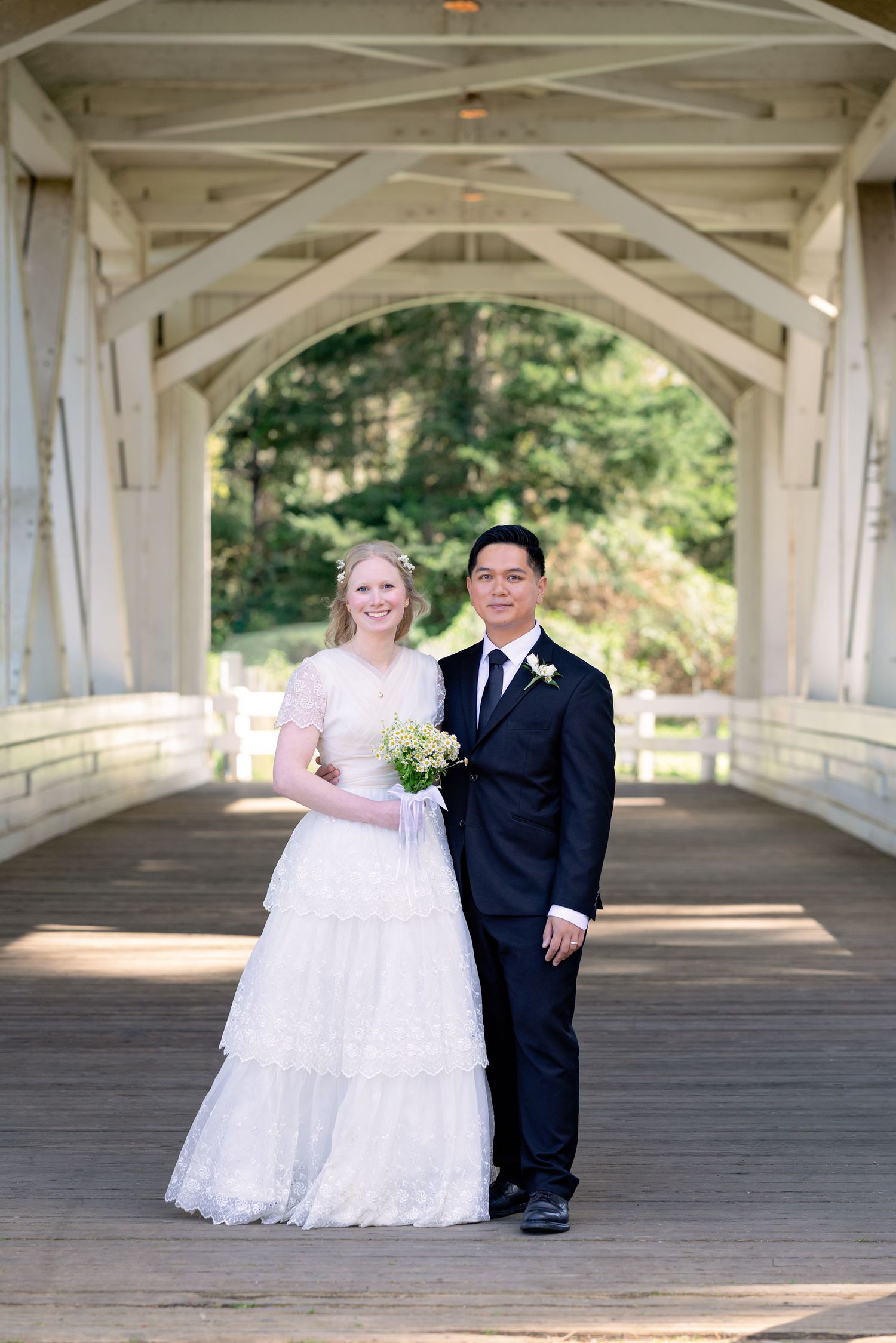 A bride and groom pose together inside a historic white covered wooden bridge on their wedding day.