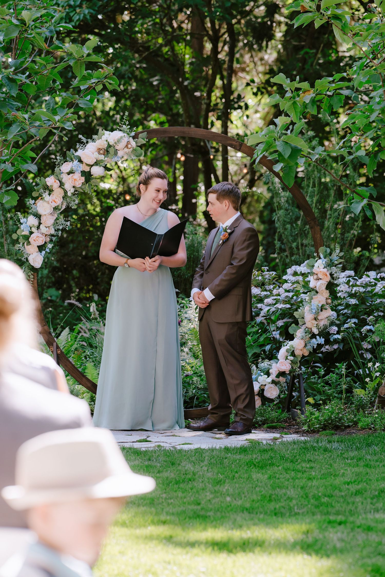 Officiant reads vows at outdoor garden wedding ceremony with floral arch.