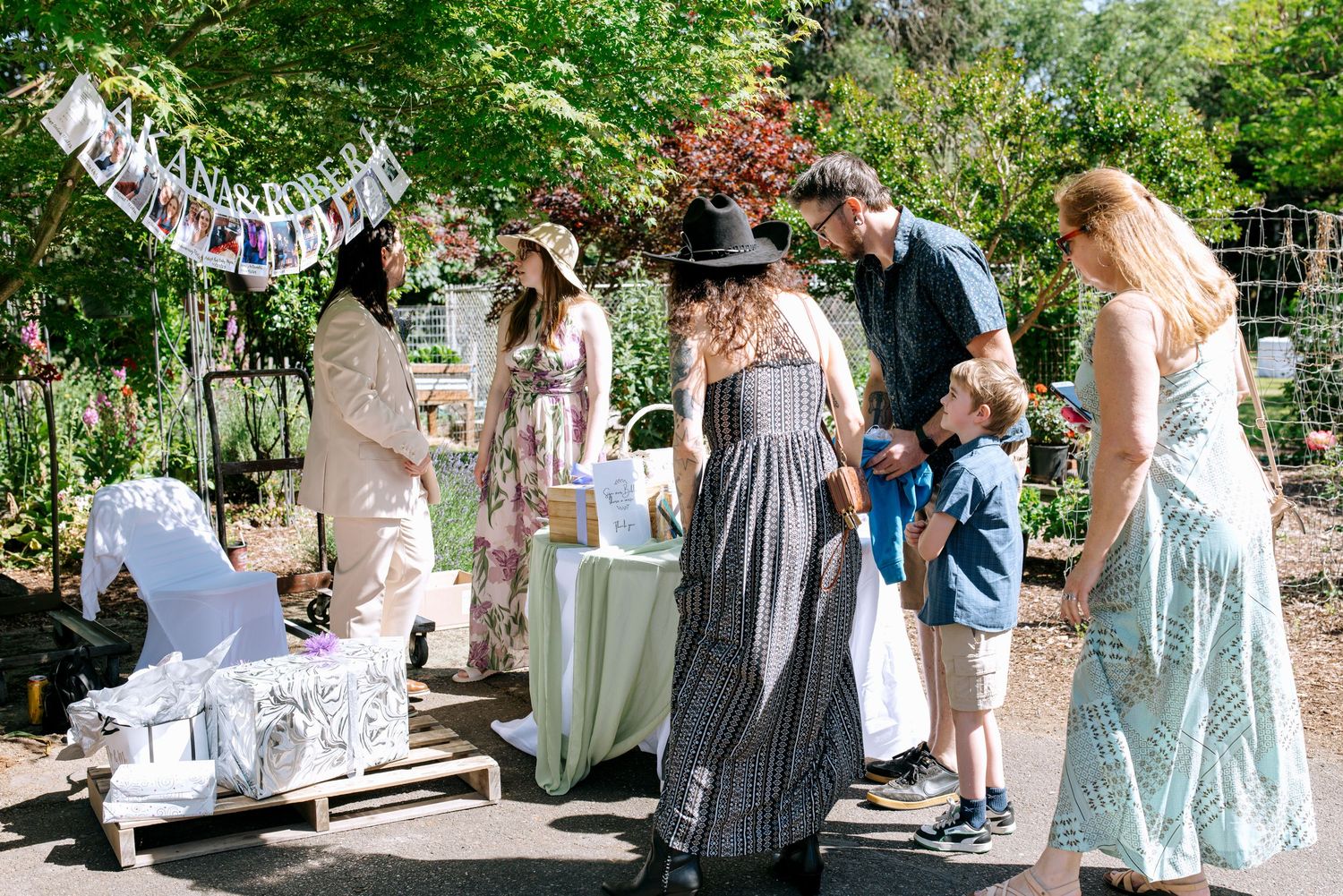 Guests mingling at an outdoor garden party with bunting decorations and a display table on a sunny day.