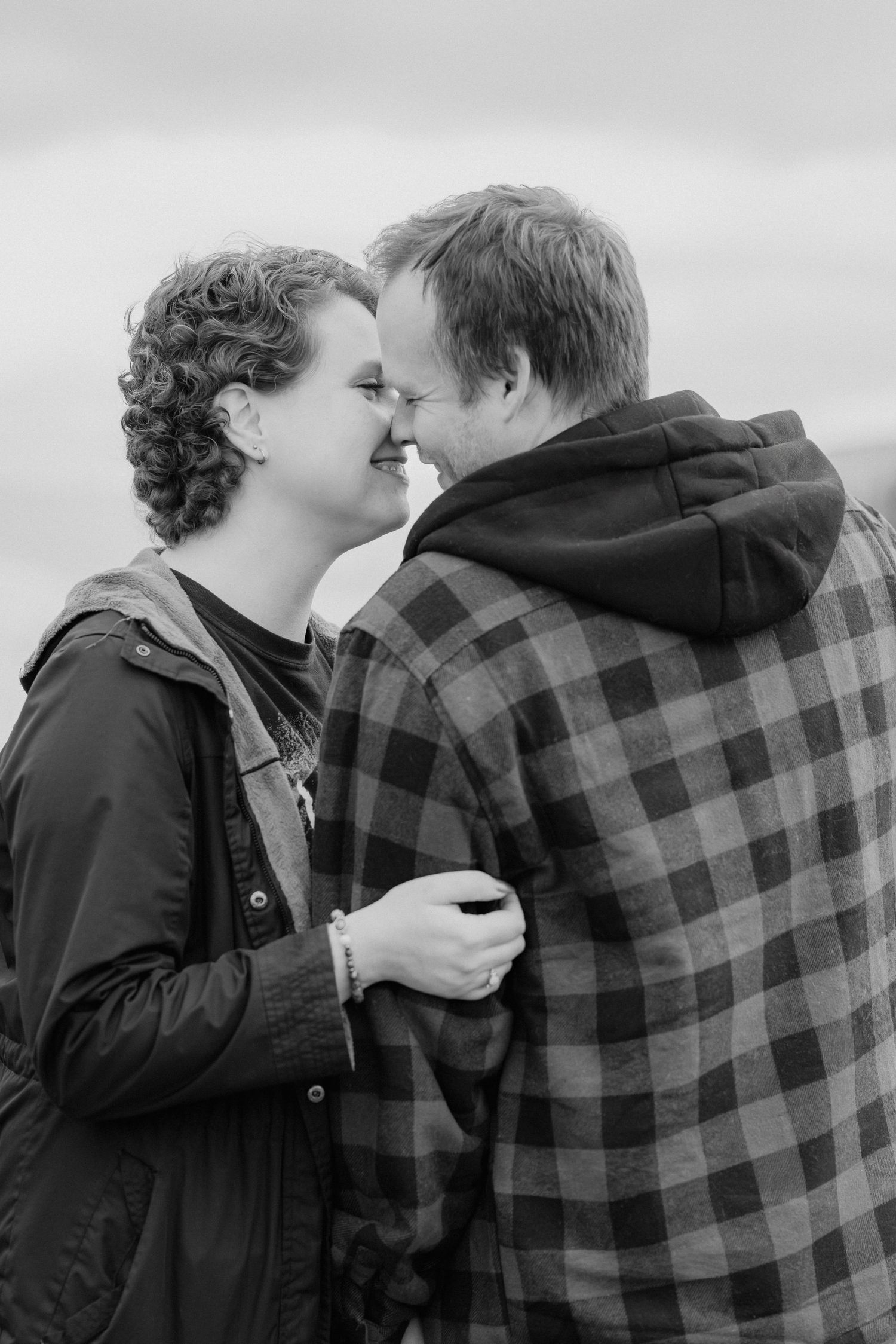 A romantic black and white portrait of a couple sharing a tender moment while wearing casual winter clothing.