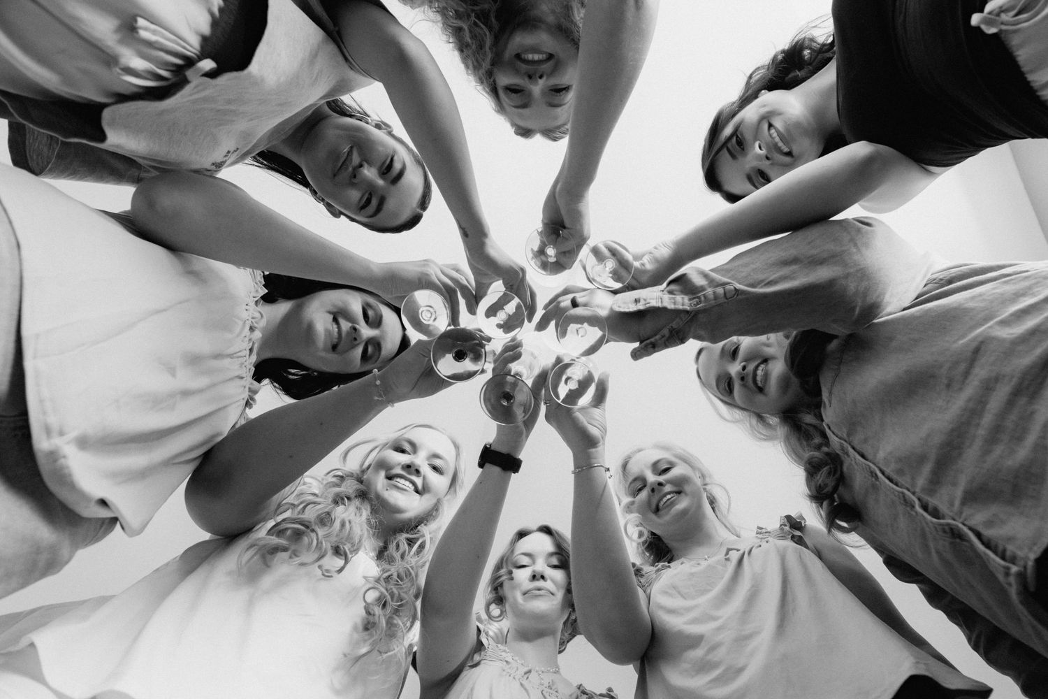 Black and white photo of a group of women in a circle huddle, reaching hands together in the center.