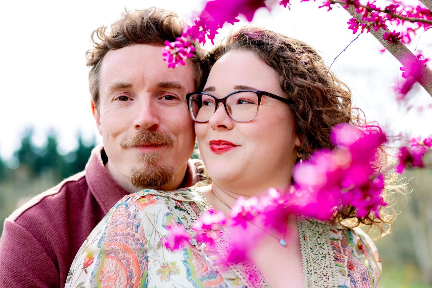 A couple shares tender moments among vibrant pink cherry blossoms in a spring engagement photo session.