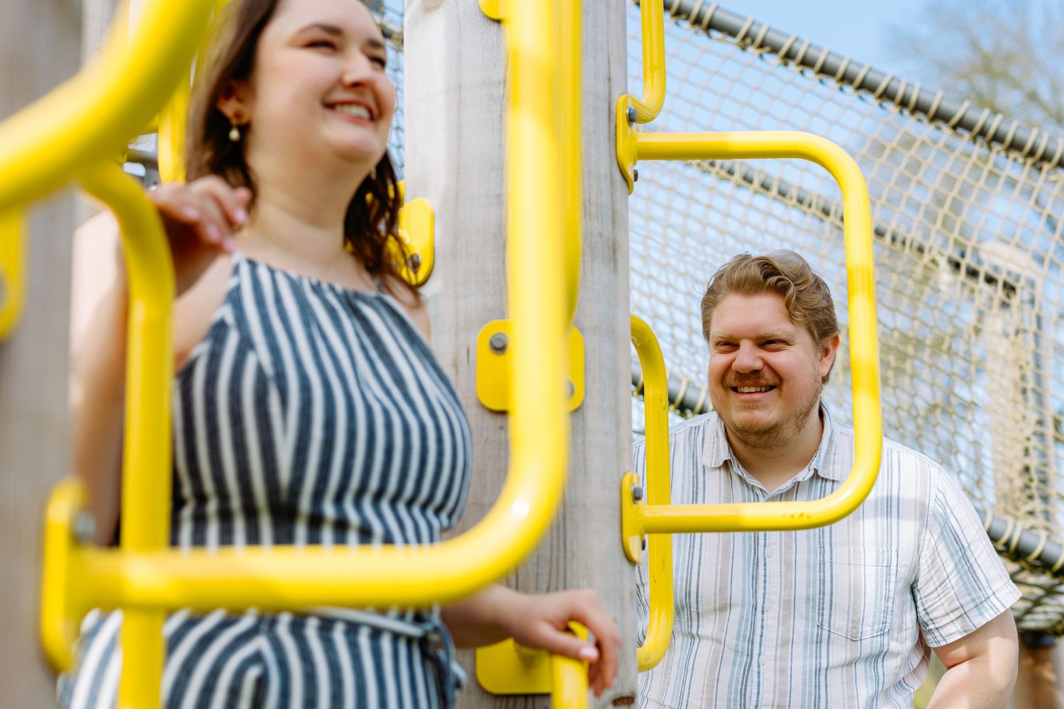 Happy couple playing on yellow playground equipment on a sunny day.
