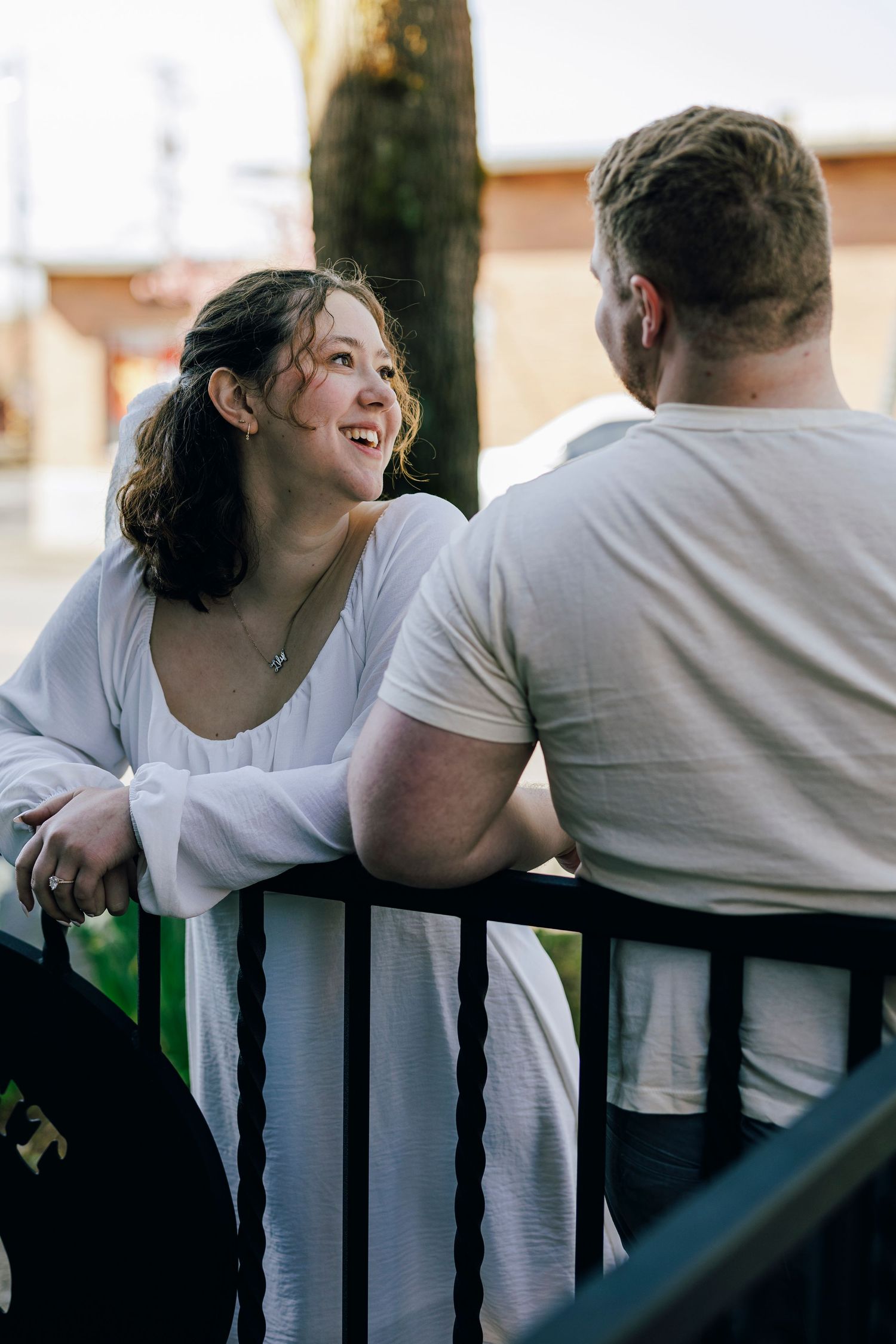 Two people having a casual conversation while leaning on a railing outdoors on a sunny day.