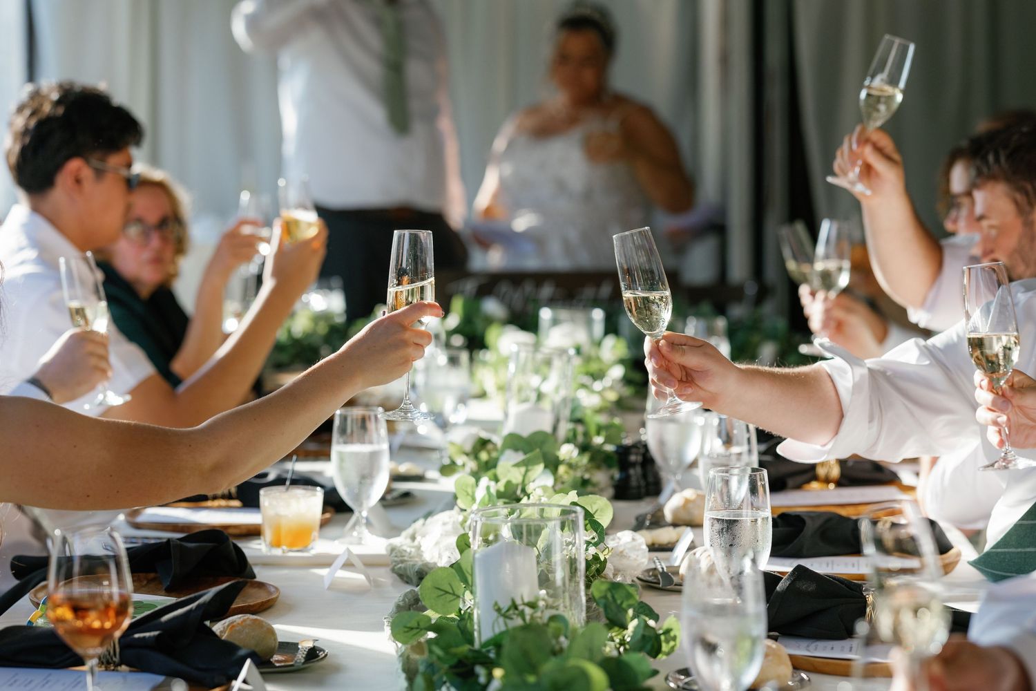Wedding reception table settings with champagne glasses and floral centerpieces during a celebration toast.