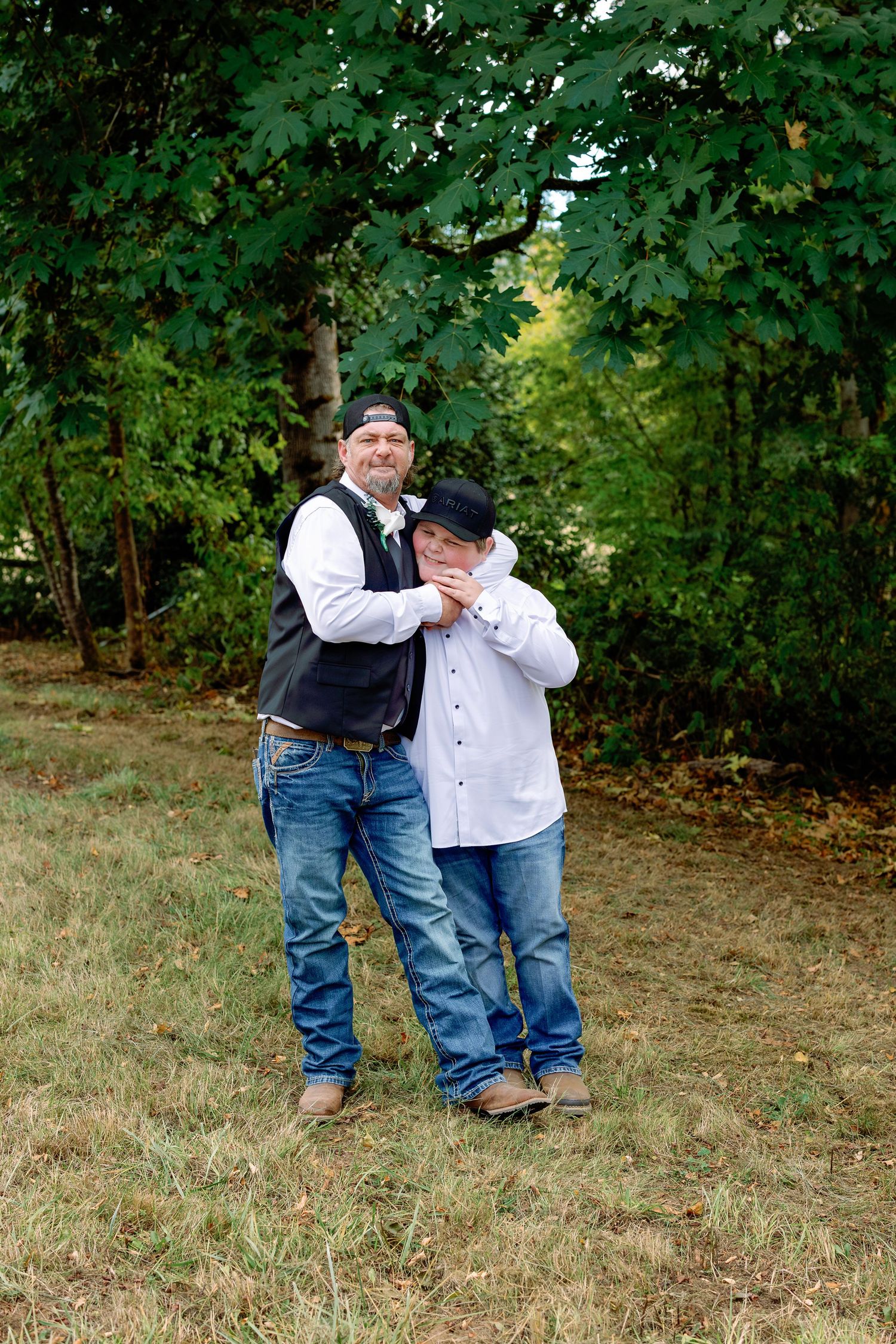 A casual outdoor photo session in a grassy area surrounded by green trees and foliage.
