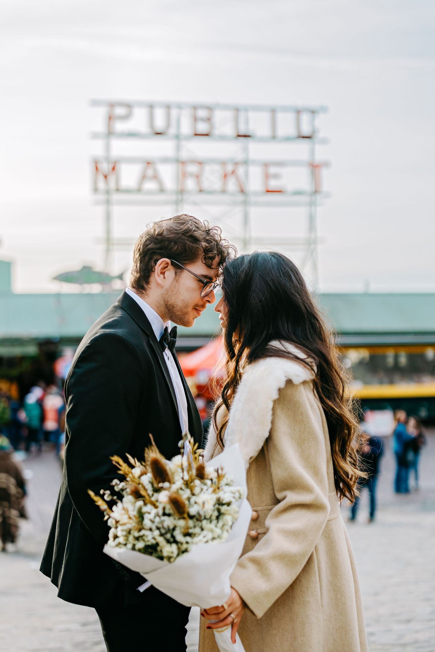 Romantic couple sharing tender moments near Pike Place Market sign with bouquet of flowers.