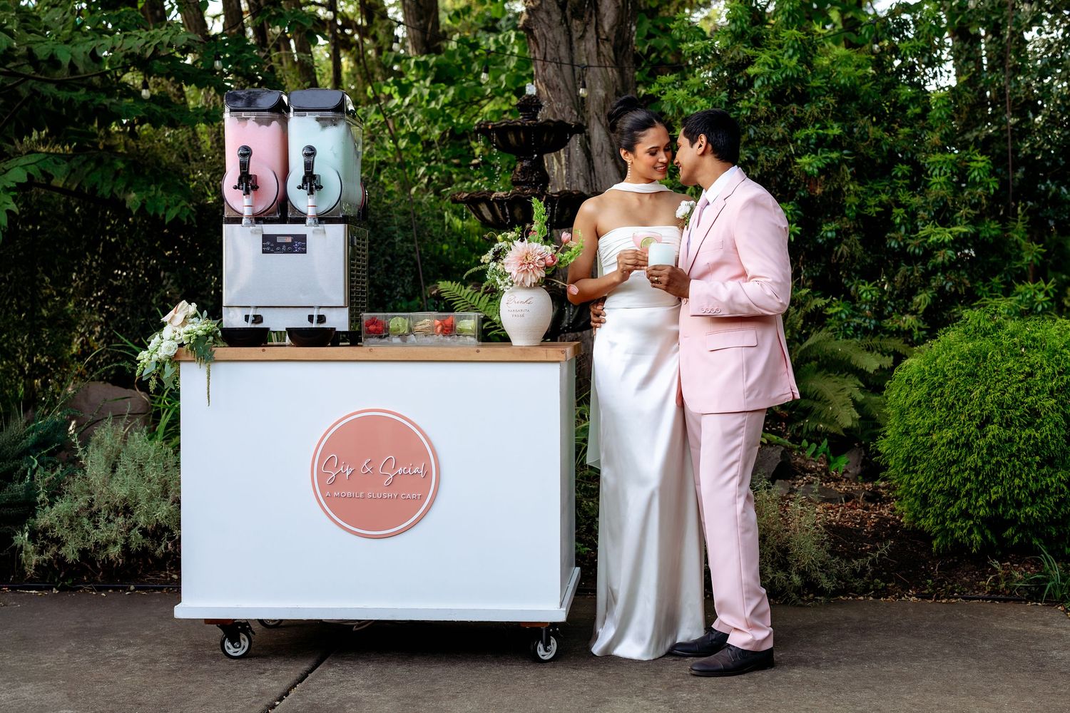 Outdoor wedding reception area with mobile beverage cart and decorative pink signage.