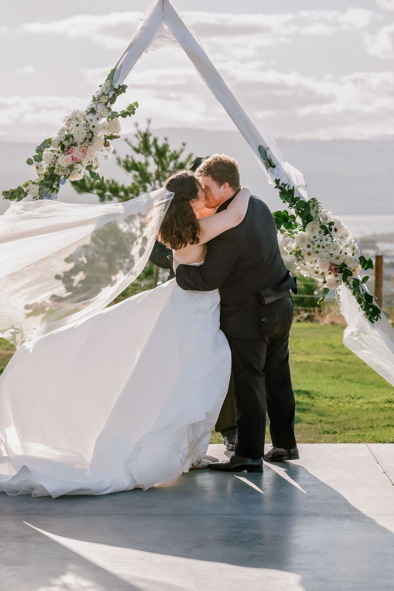 Wedding couple sharing romantic moments under floral arch during outdoor ceremony.