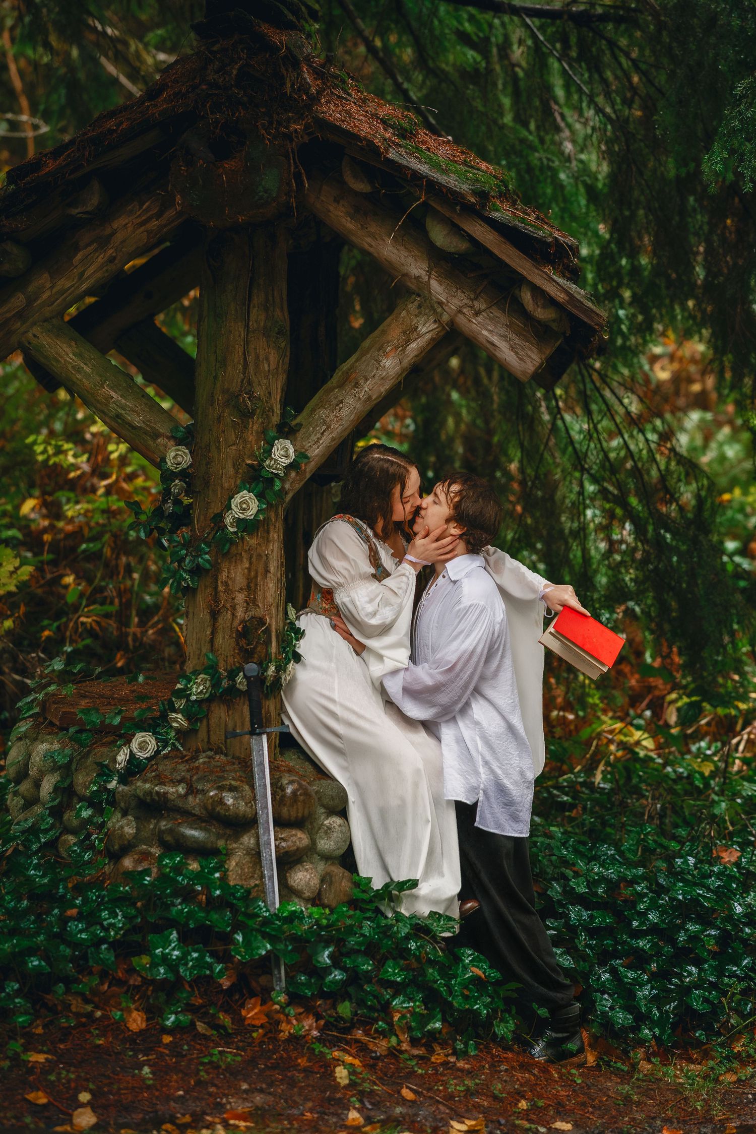 A couple in white clothing shares an intimate moment under a rustic wooden structure.