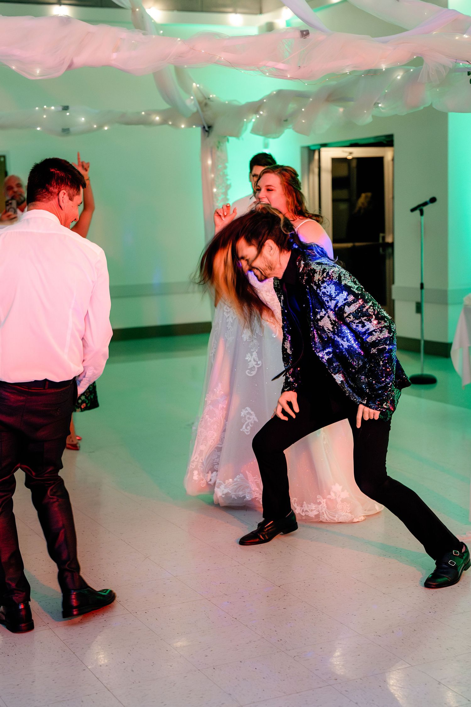 Wedding guests dancing energetically under colorful lighting at a reception party.