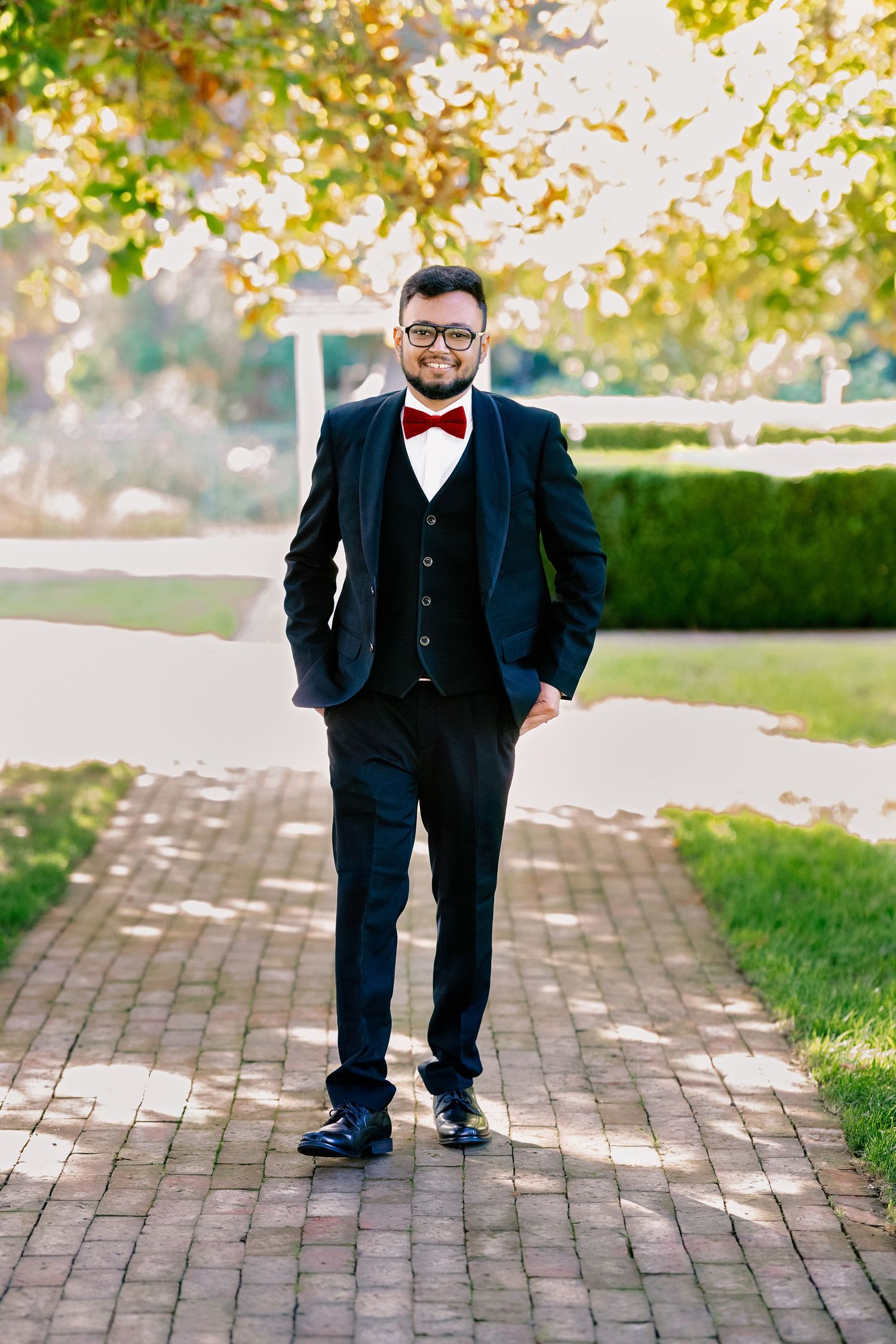 A series of playful poses on a brick pathway showing a dapper outfit with a bow tie and dark suit.