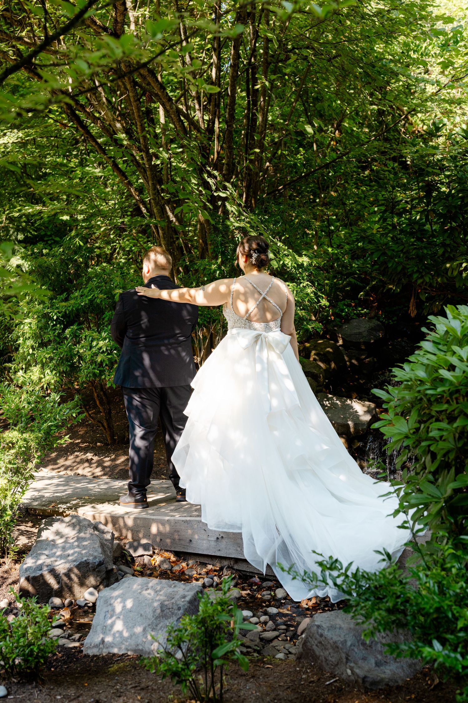 Bride and groom walking hand-in-hand up stone steps through a lush green garden on their wedding day.