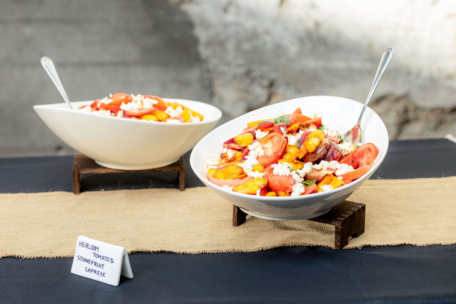 Two white bowls filled with colorful heirloom tomato salad served on a burlap table runner.