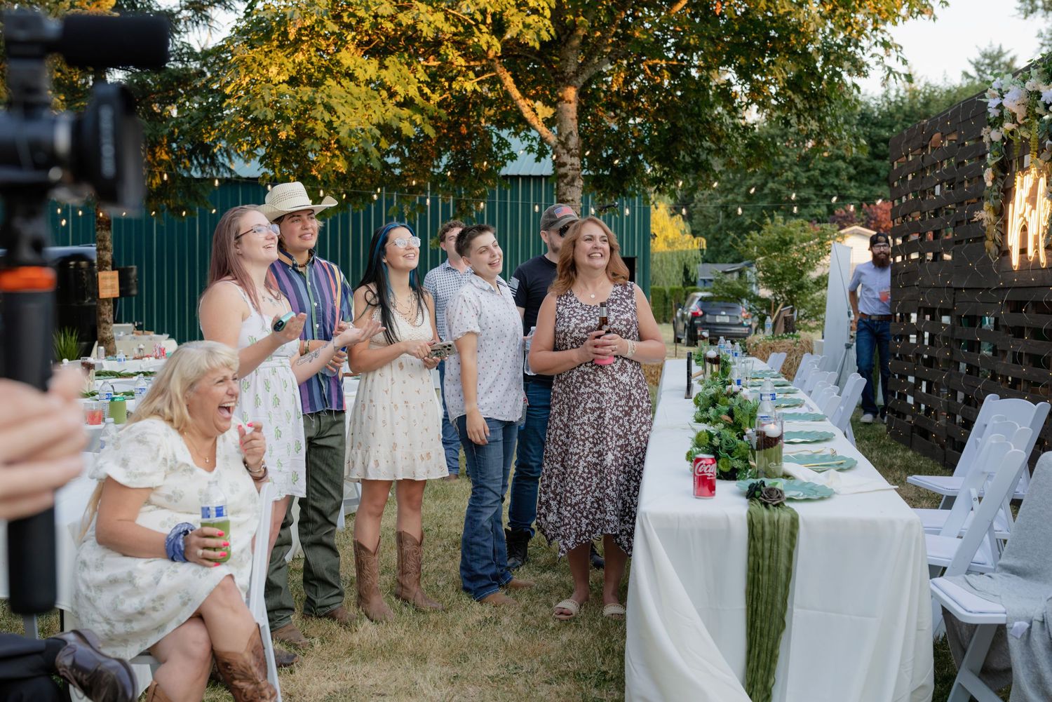 Wedding guests laugh and mingle outdoors beside a long decorated reception dinner table.