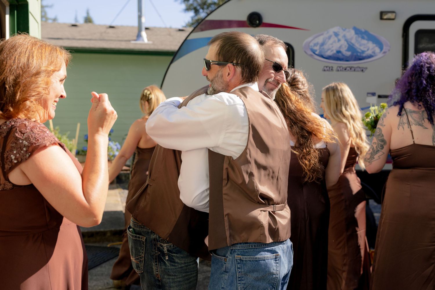 Wedding guests hugging and celebrating outdoors near a vintage trailer after a ceremony.