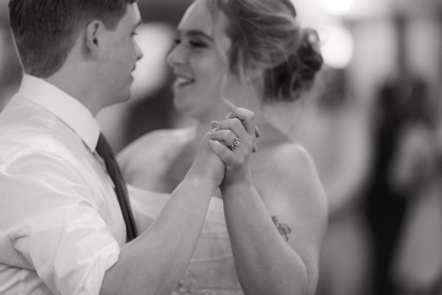 Black and white photo of bride and groom sharing first dance holding hands closely.
