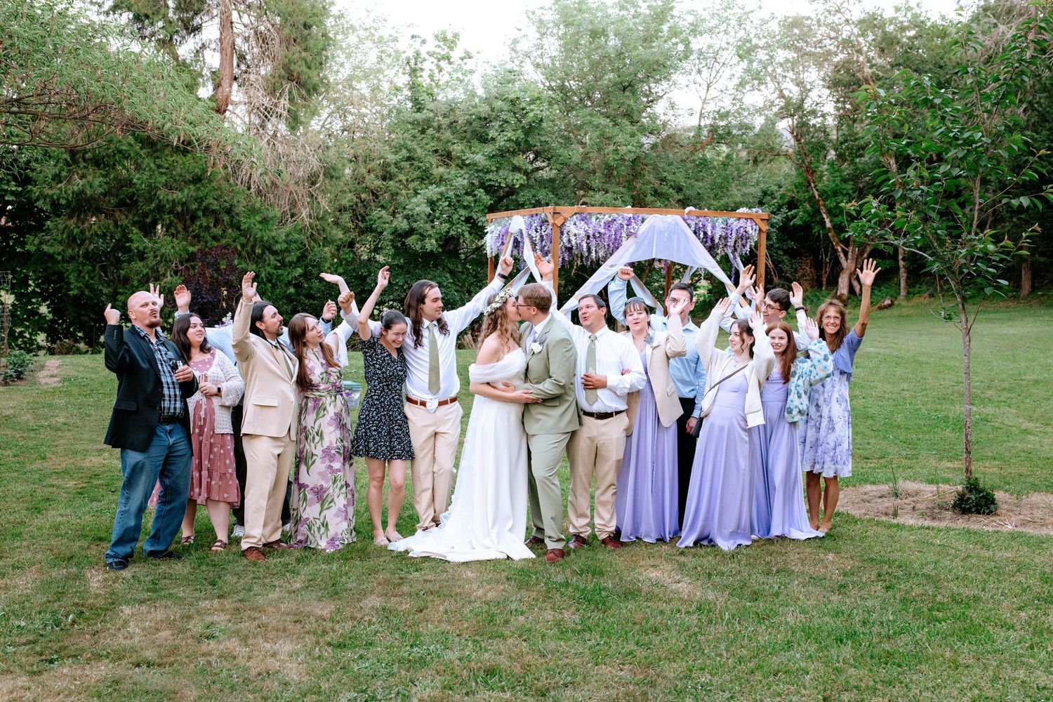 Wedding party celebrating under a floral arch in a lush garden setting.